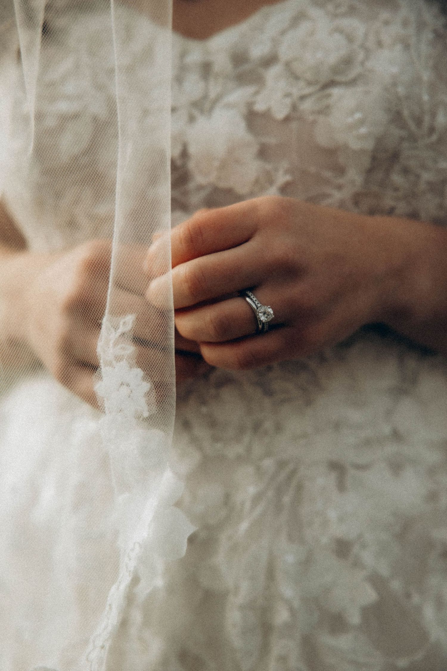 Close-up of delicate lace details and an engagement ring in soft lighting.