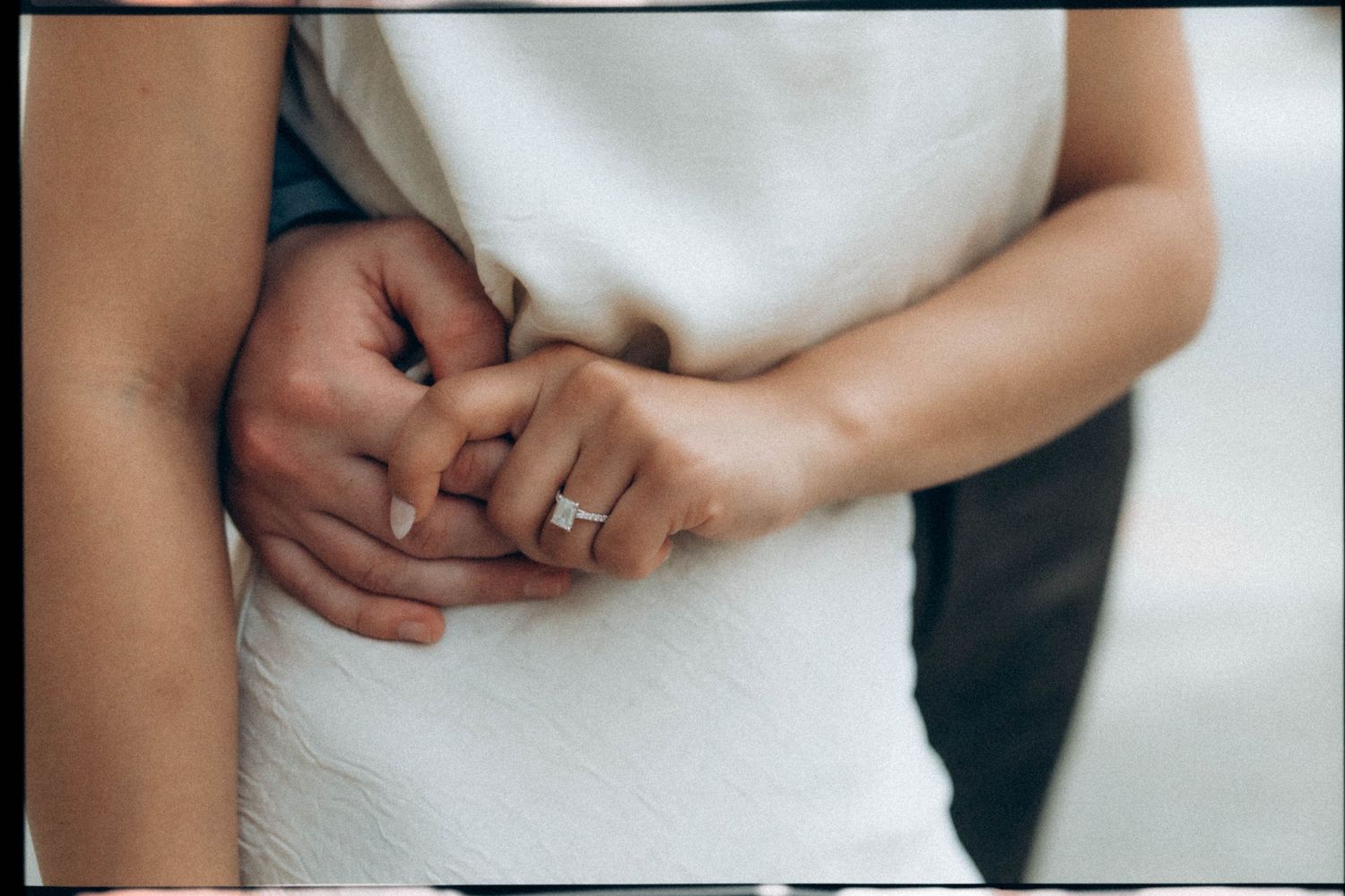Close-up of hands with wedding ring detail in soft white lighting.