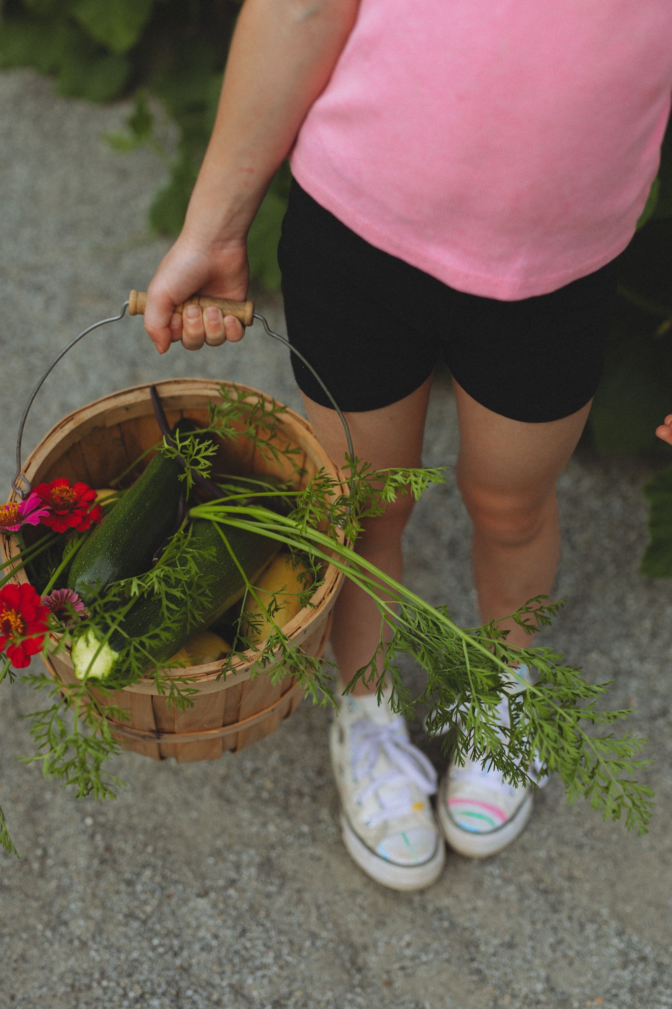 Close-up of hands holding woven basket filled with freshly picked flowers and greenery.