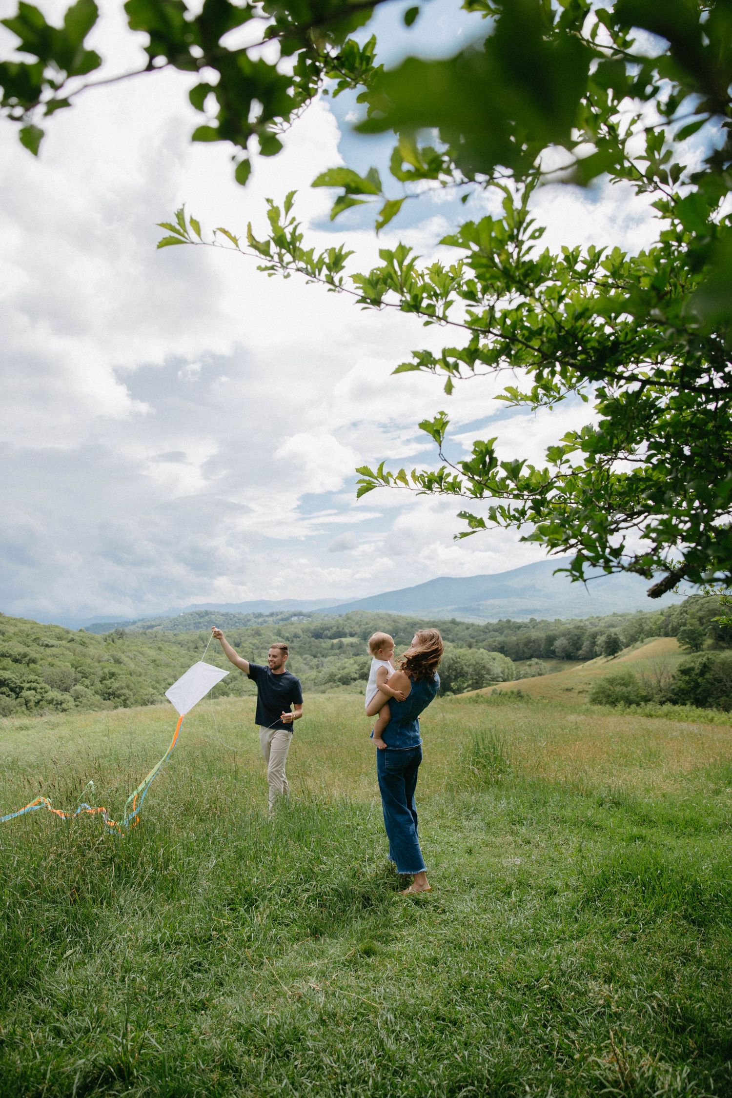 Three people toss papers into the air while standing in a lush green meadow with mountains in the background.