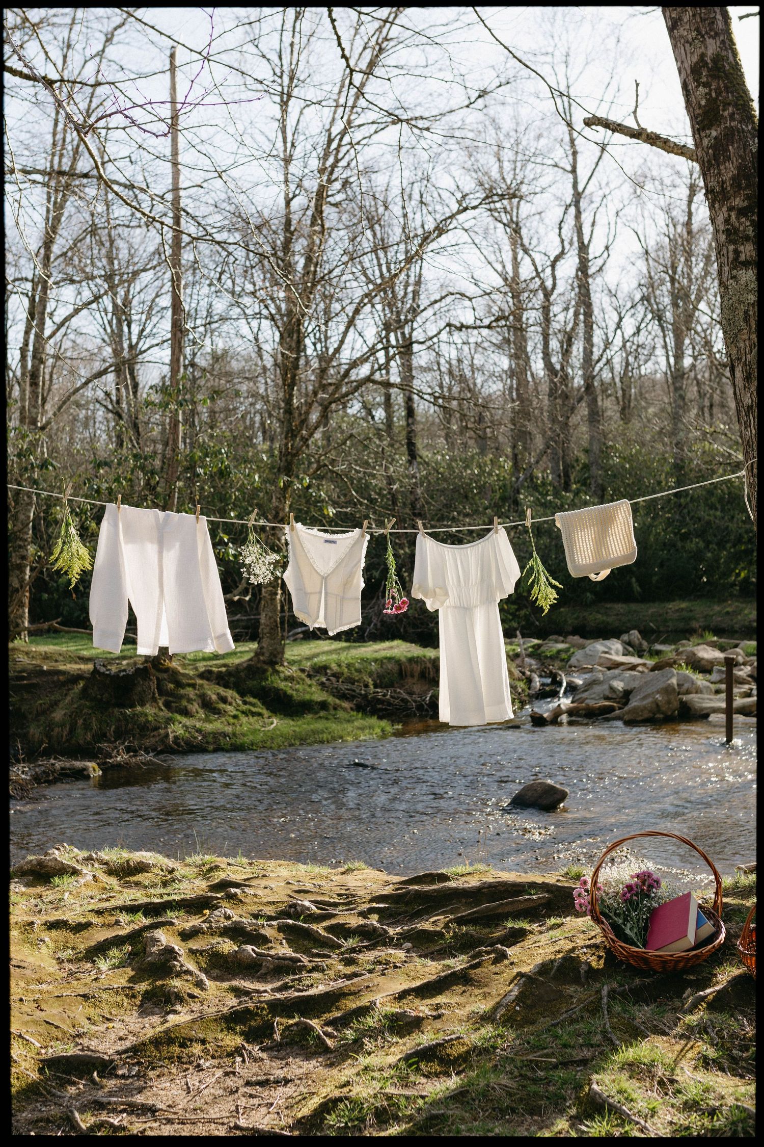Freshly washed white laundry hanging on clothesline outdoors against wooded creek landscape.