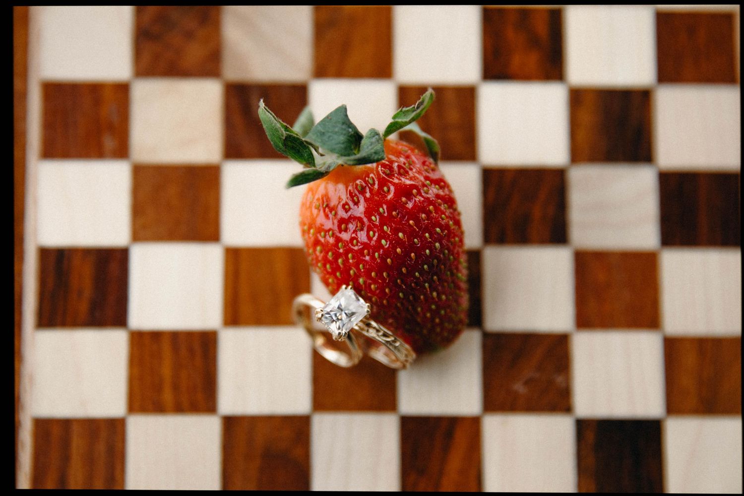 Fresh red strawberries arranged on wooden checkerboard pattern surface.