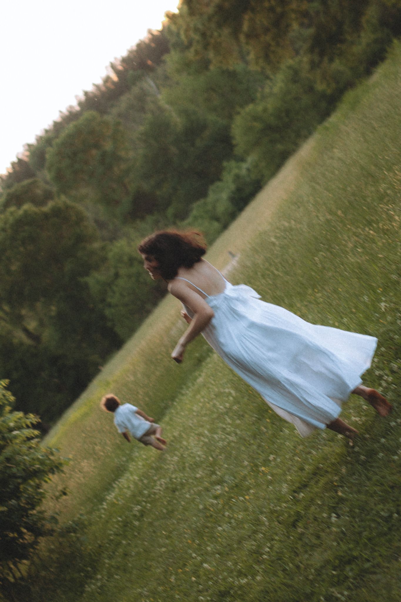 A dreamy scene of a figure in a light blue dress dancing in a grassy field at sunset.