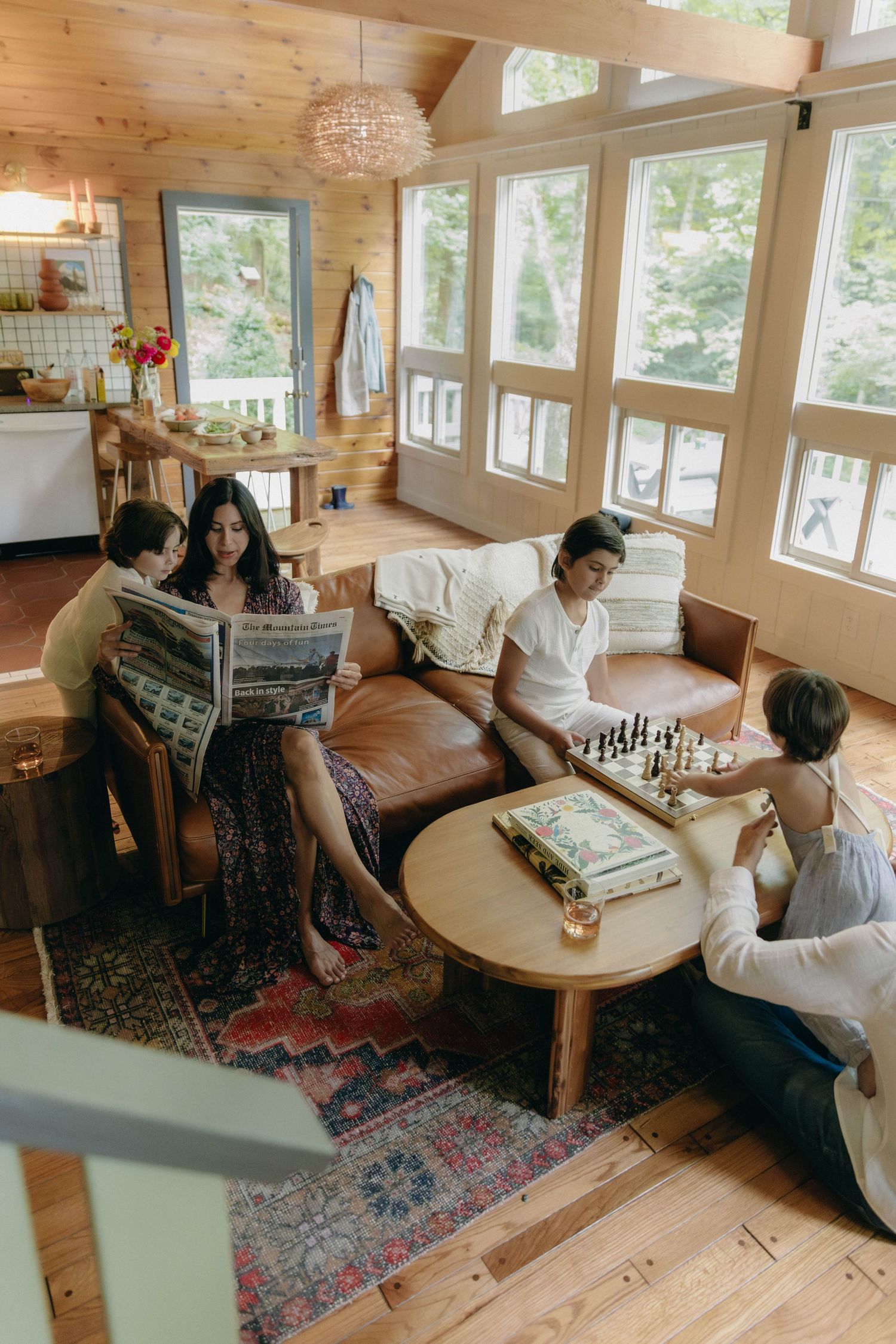 People relaxing and playing board games in a cozy wood-paneled cabin with large windows and natural lighting.