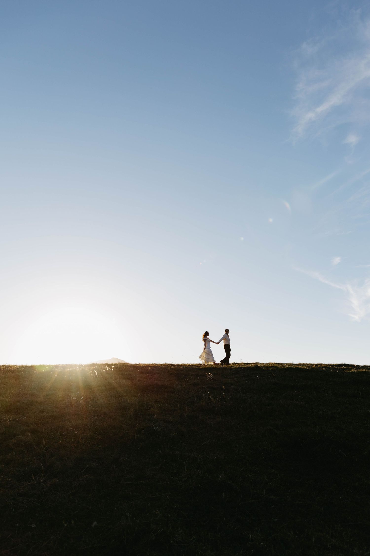 Silhouetted figures stand on a hilltop against a bright sunset sky creating a romantic panoramic view.