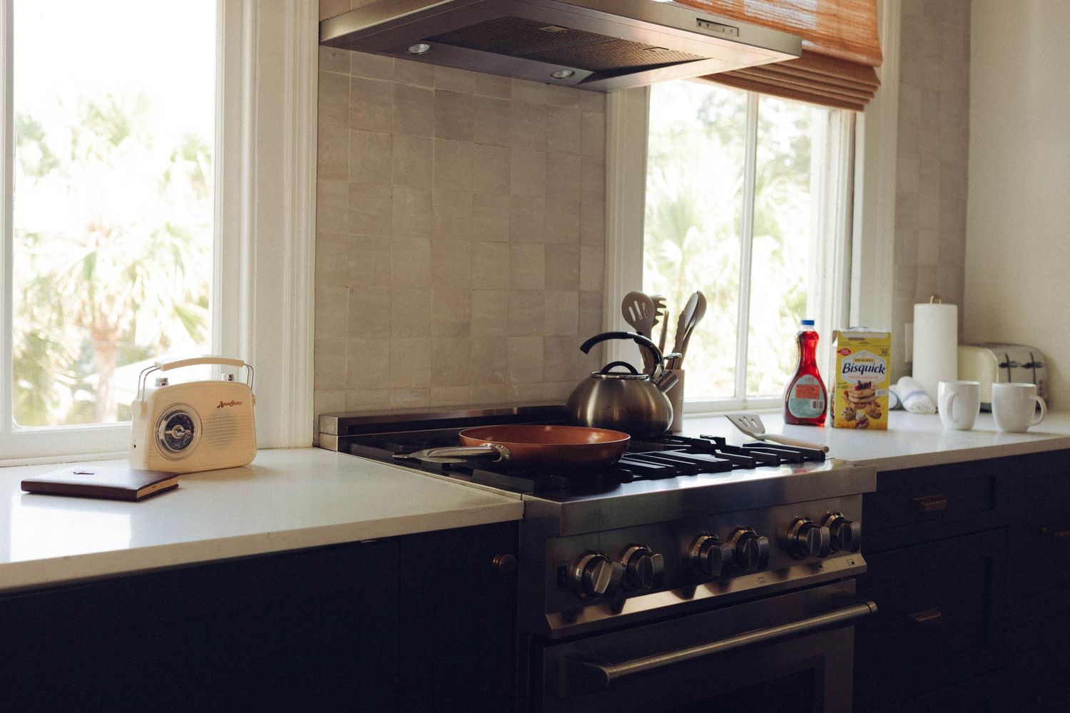 Modern kitchen interior with white cabinets and large windows letting in natural light.