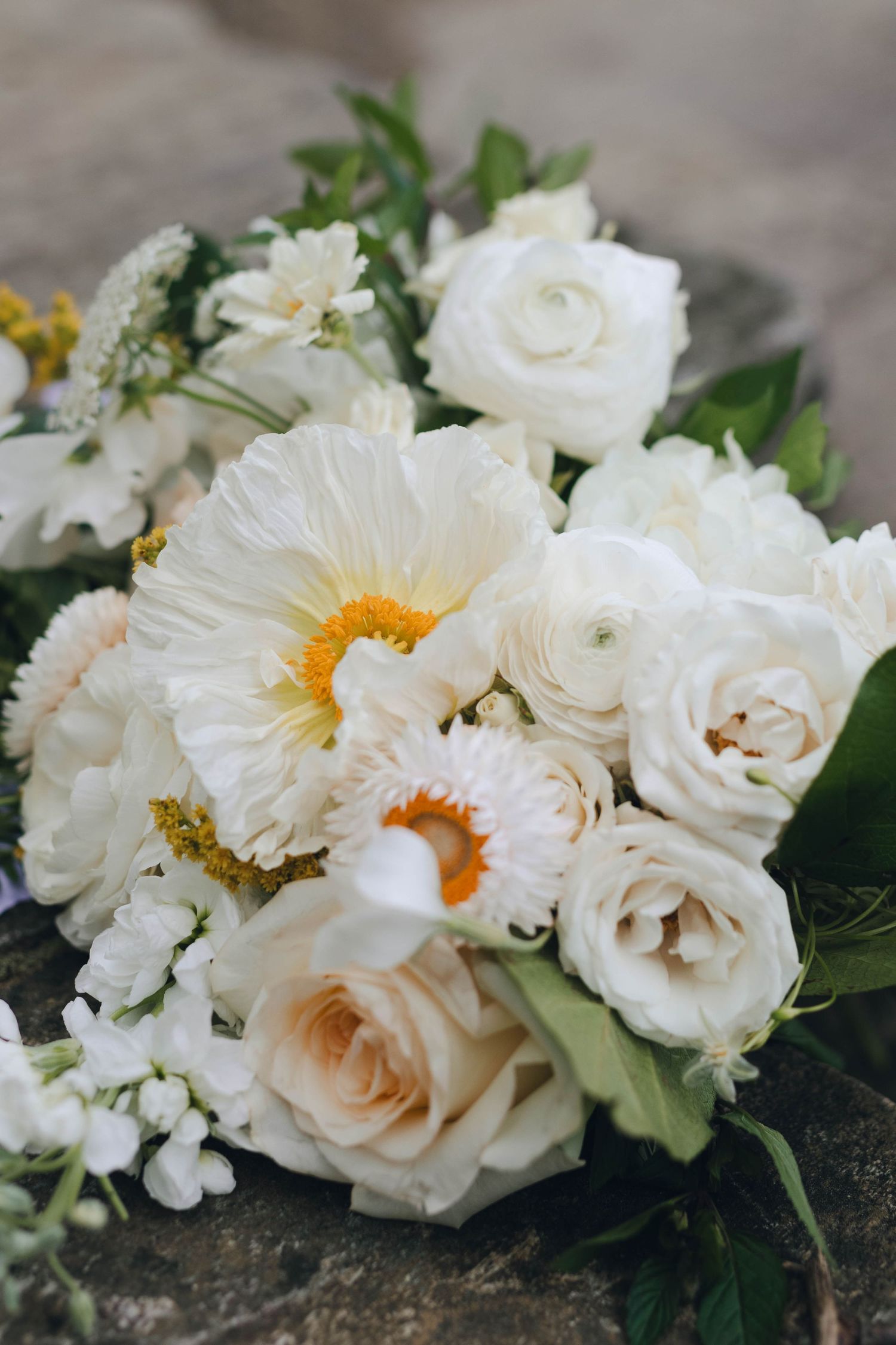 Delicate white roses and flowers arranged in an elegant display with green foliage against a textured surface.