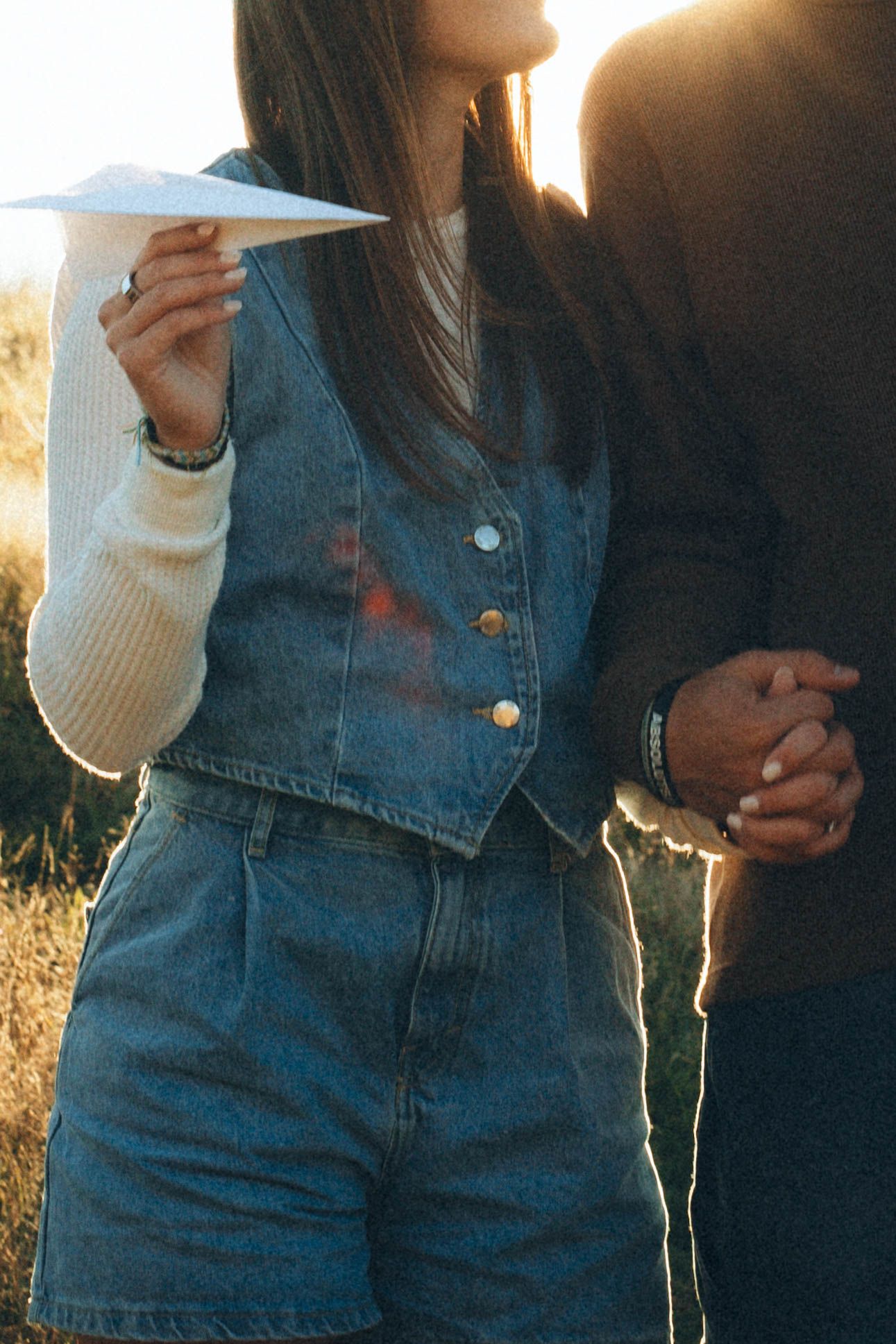 Close-up shots of someone wearing denim overalls and a white sweater in golden sunlight.