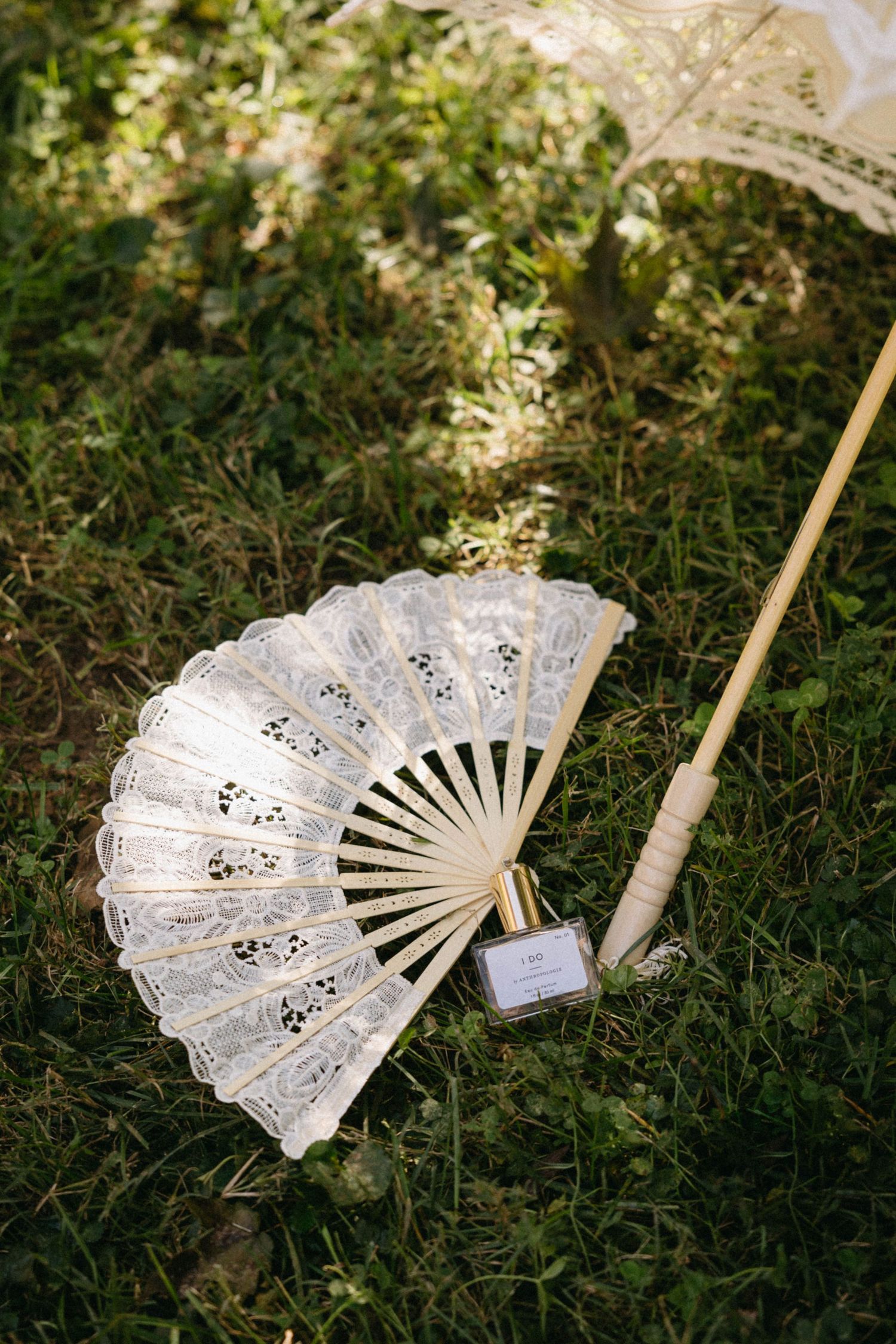 A delicate white lace hand fan with intricate floral patterns lies on green grass in natural lighting.