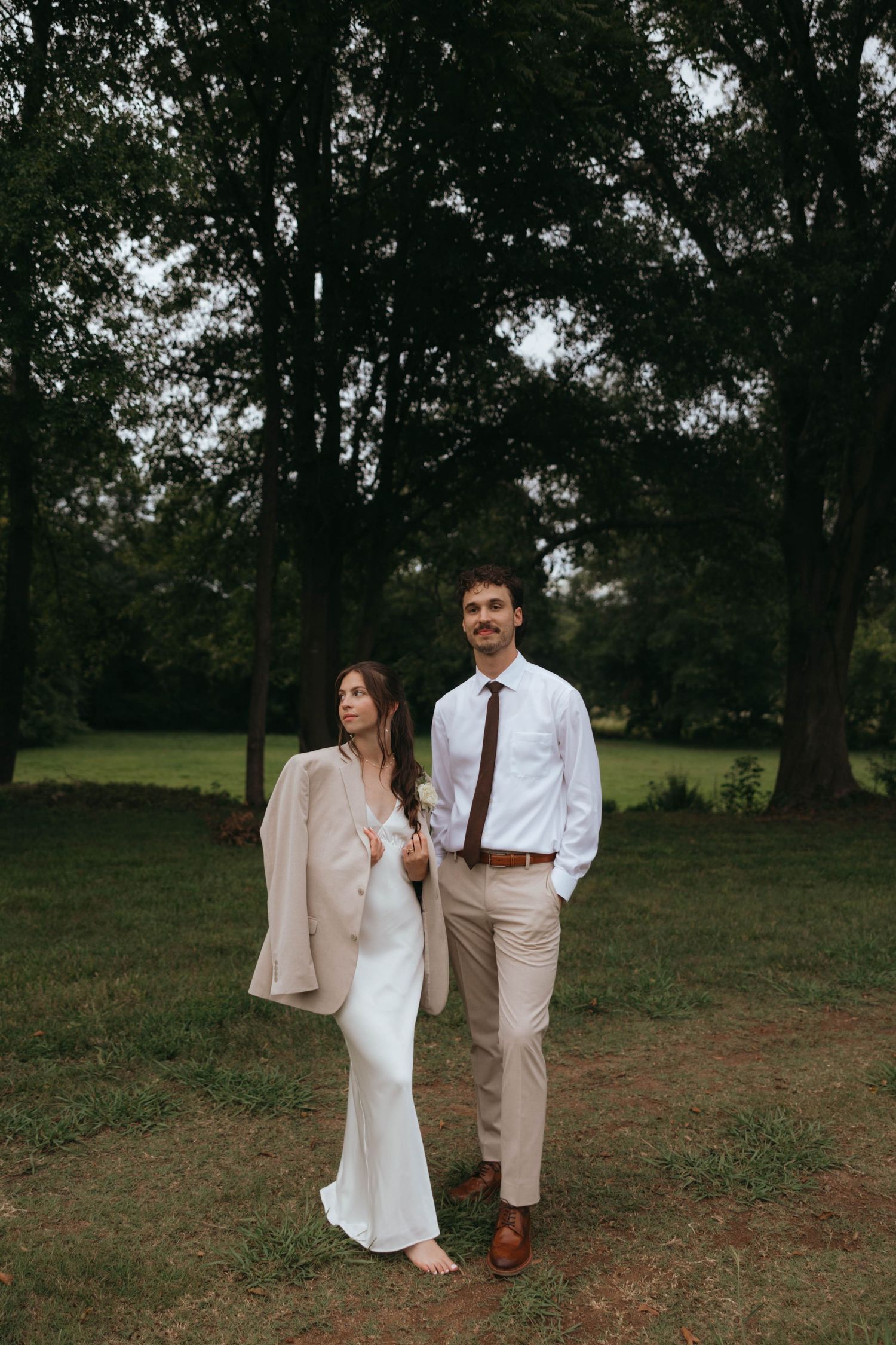 Couple walking together through a rustic outdoor setting wearing light colored clothing.