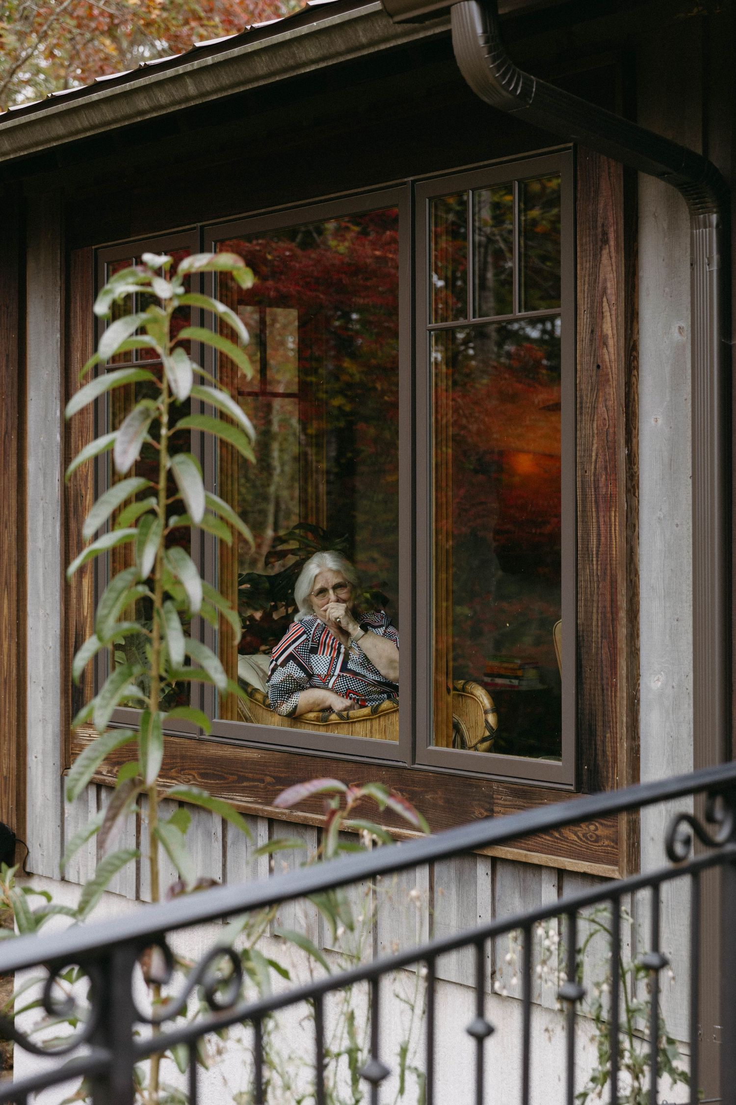 Through a window of a cozy home, autumn foliage creates a warm backdrop as someone relaxes in a comfortable interior space.