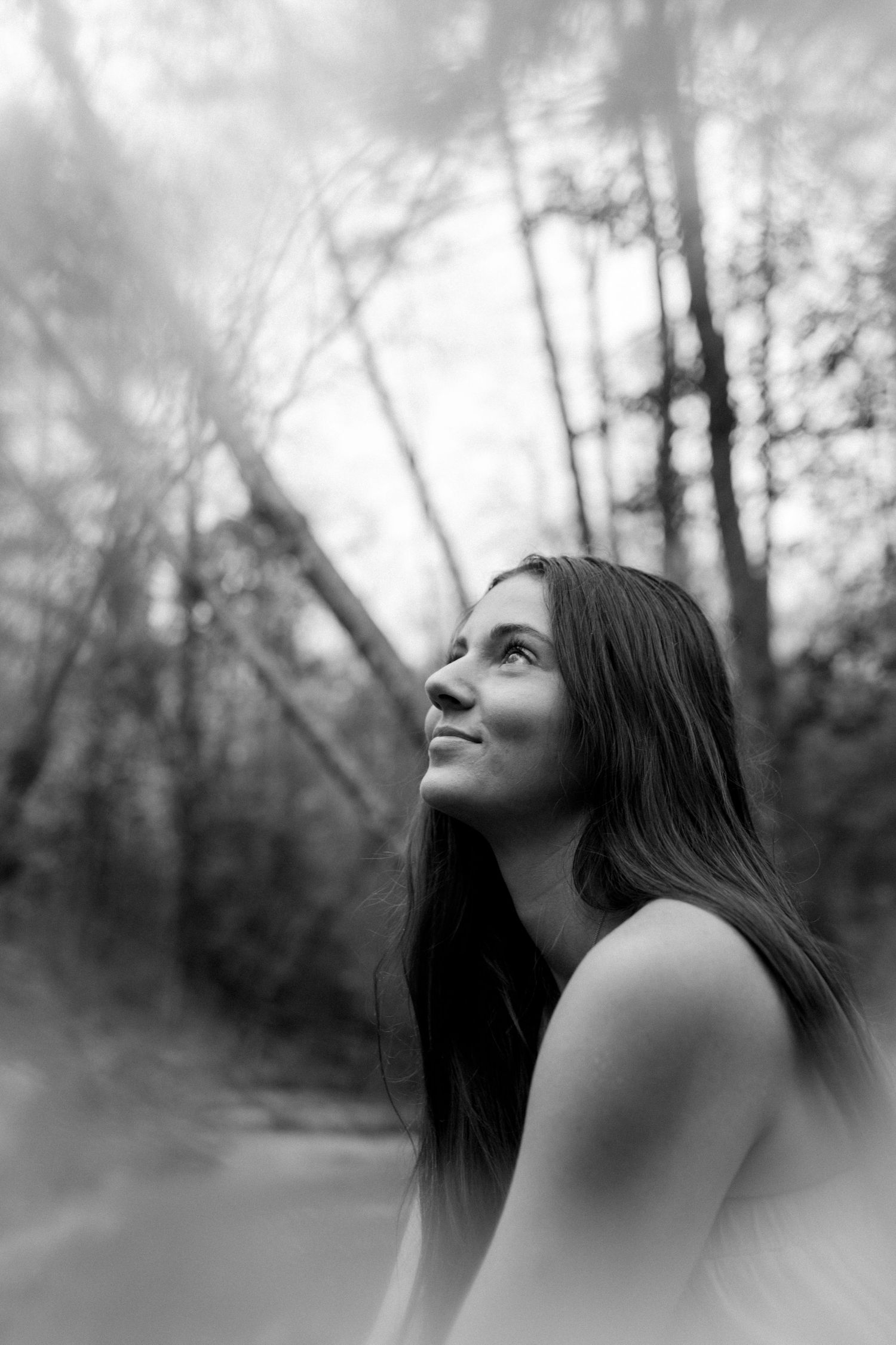 Artistic black and white portrait showing upward gaze against a blurred forest background.