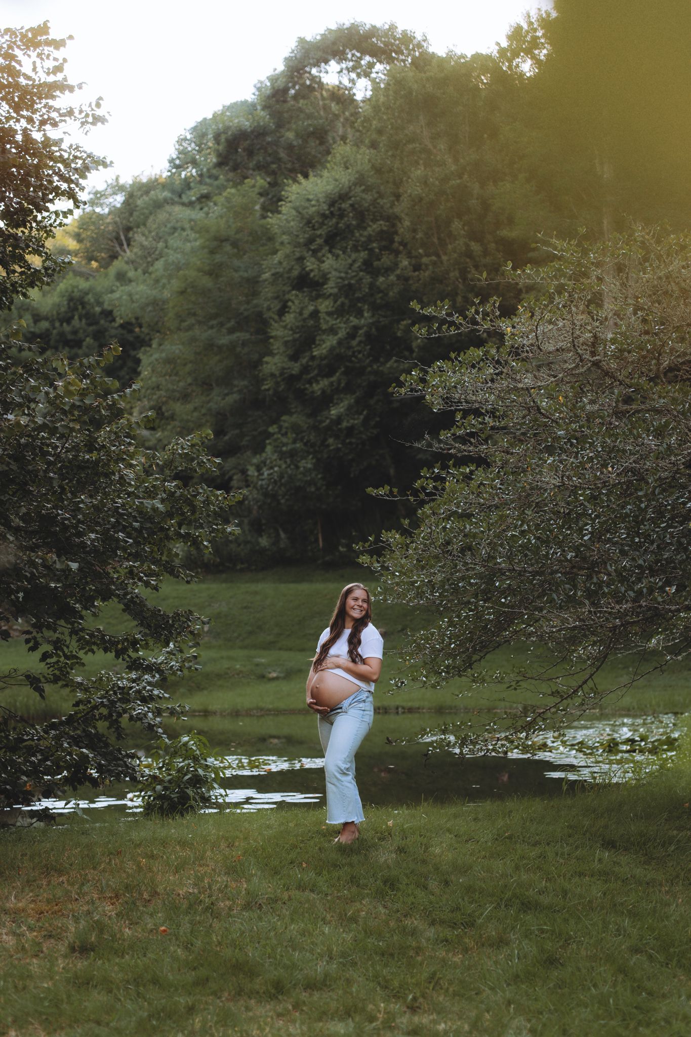 Person in white dress posing among trees in sunset-lit garden setting.