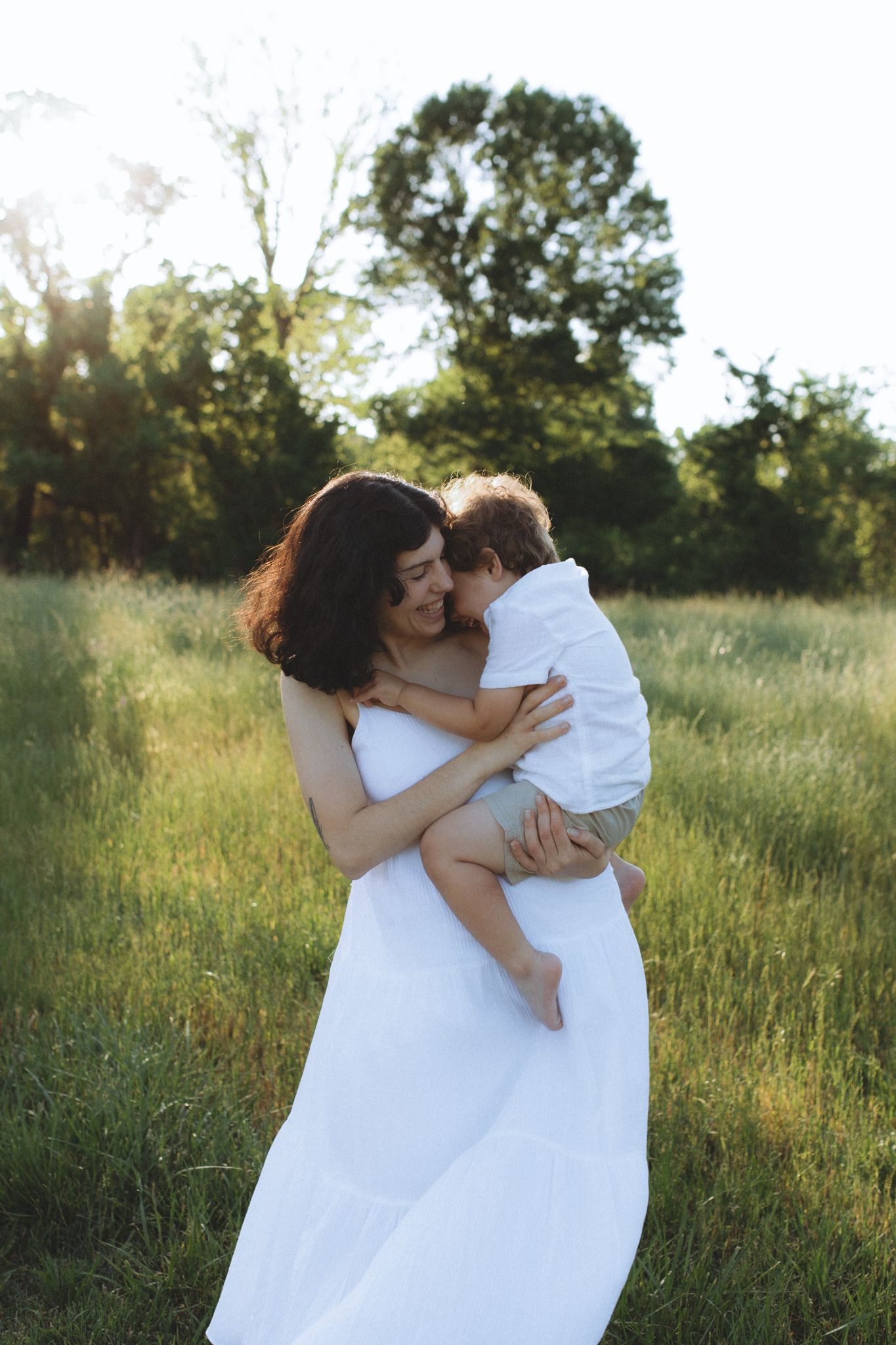 An intimate outdoor portrait showing tender embrace between parent and child in a sunlit meadow.