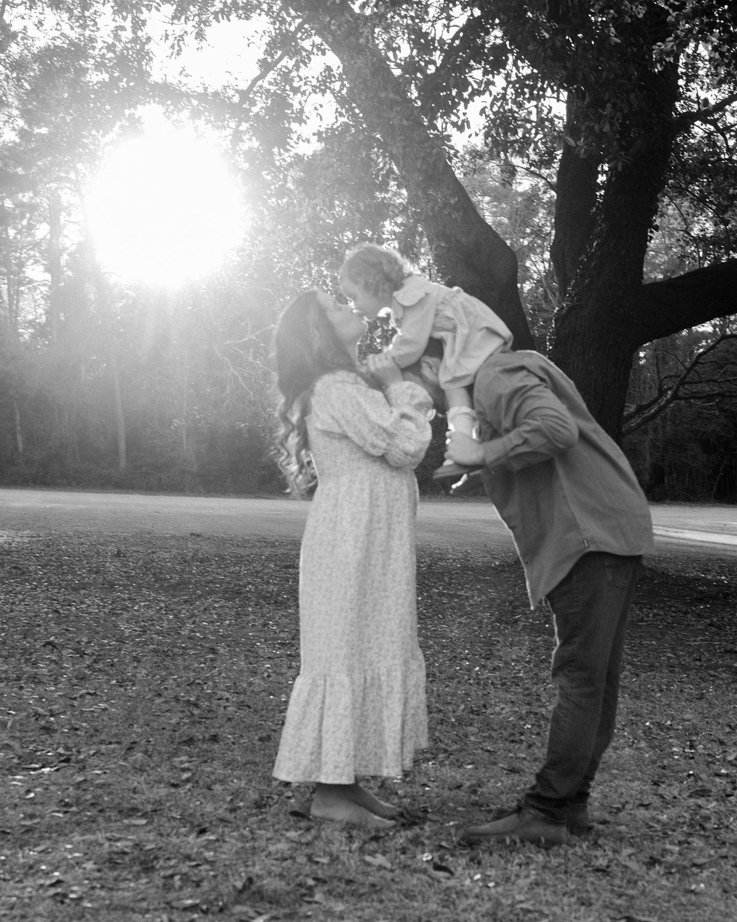 A couple dancing together in a park with dramatic sunlight filtering through the trees.