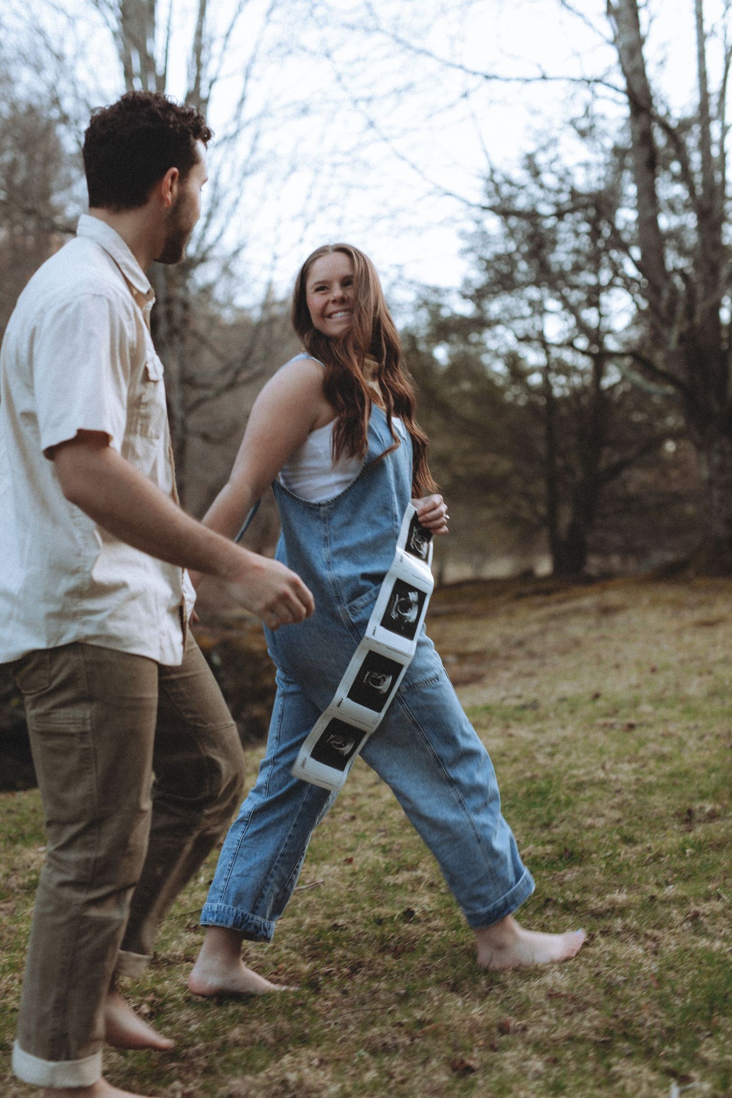 A playful couple dancing barefoot on a grassy hillside on a sunny afternoon.