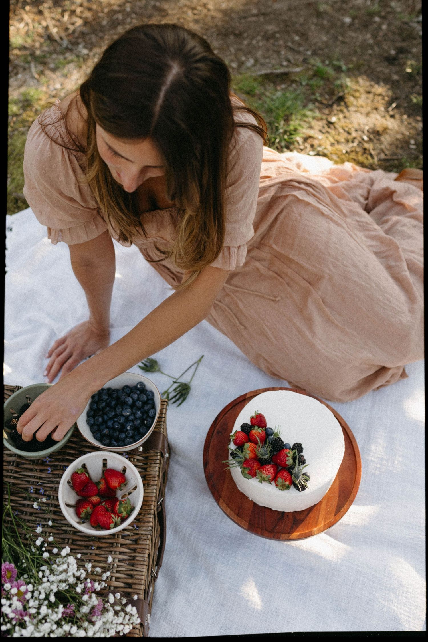 Arranging fresh berries and flowers on white linen for a rustic outdoor setting.