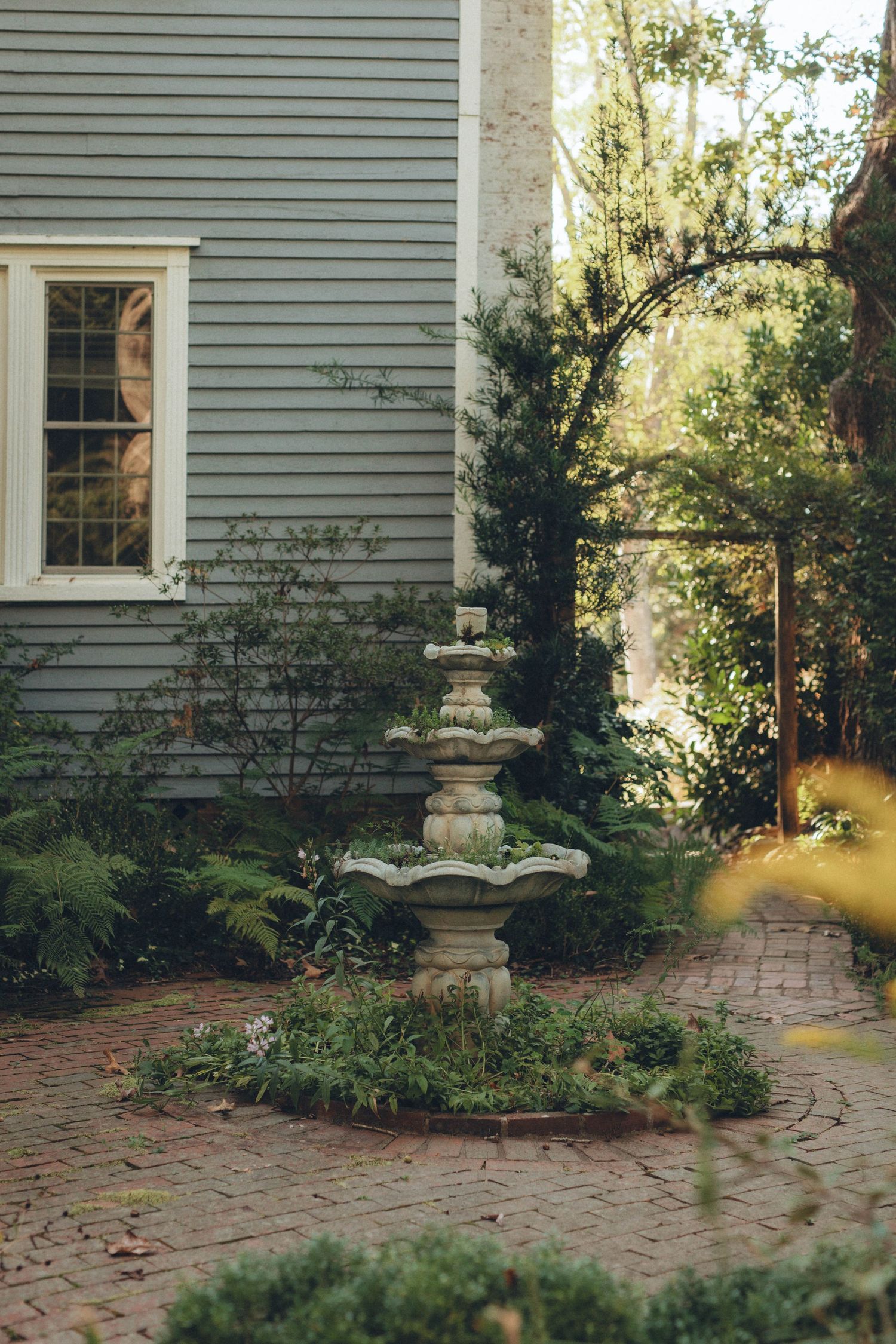 White clapboard house with brick pathway and garden features in natural sunlight.