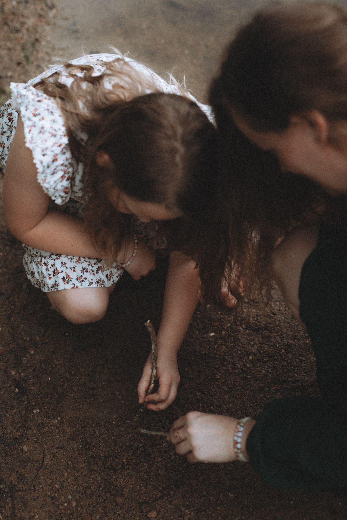 Two people kneeling on the ground examining something in the dirt together.