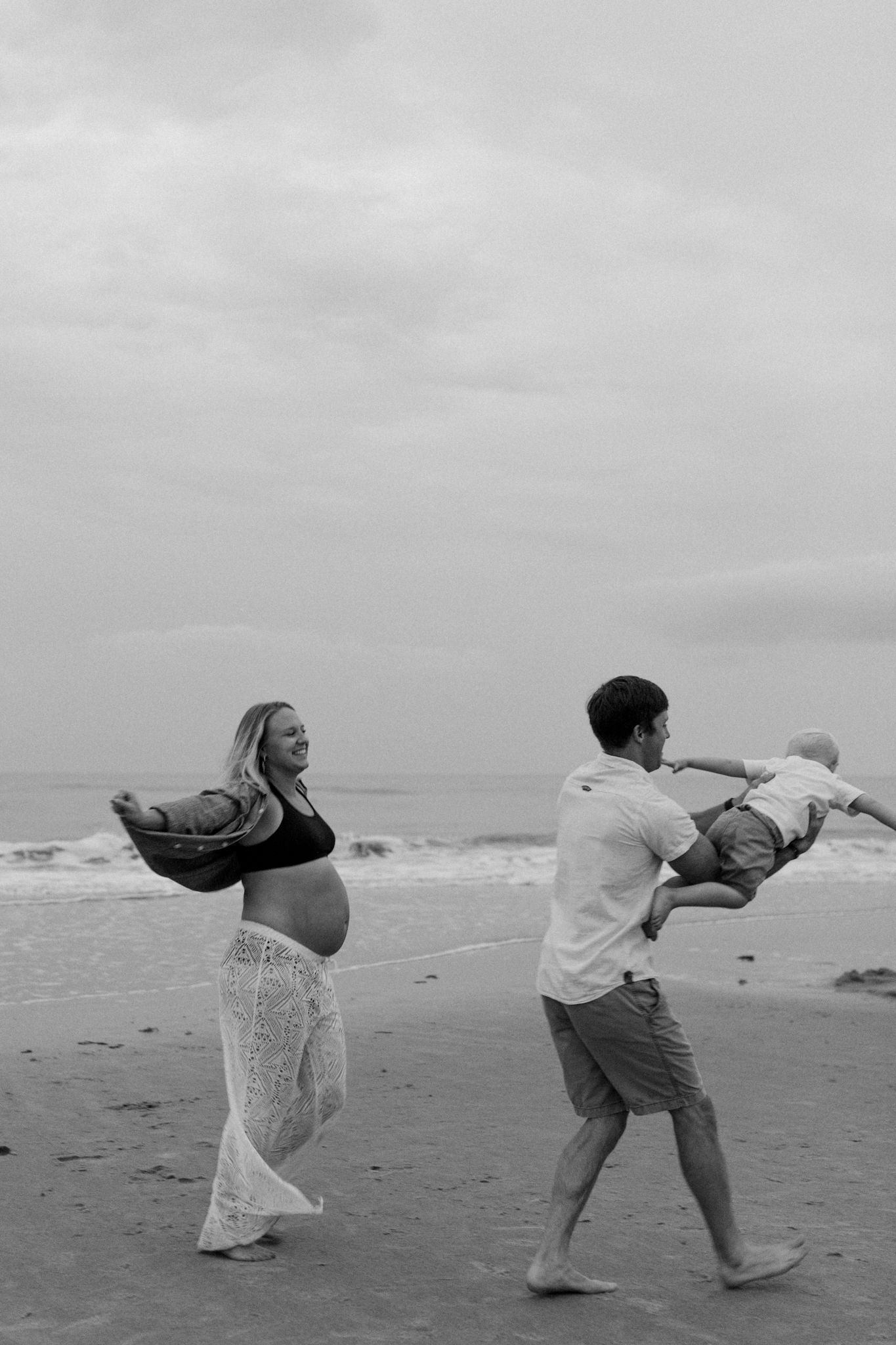 A couple playfully posing on a beach in black and white, creating dynamic silhouettes.