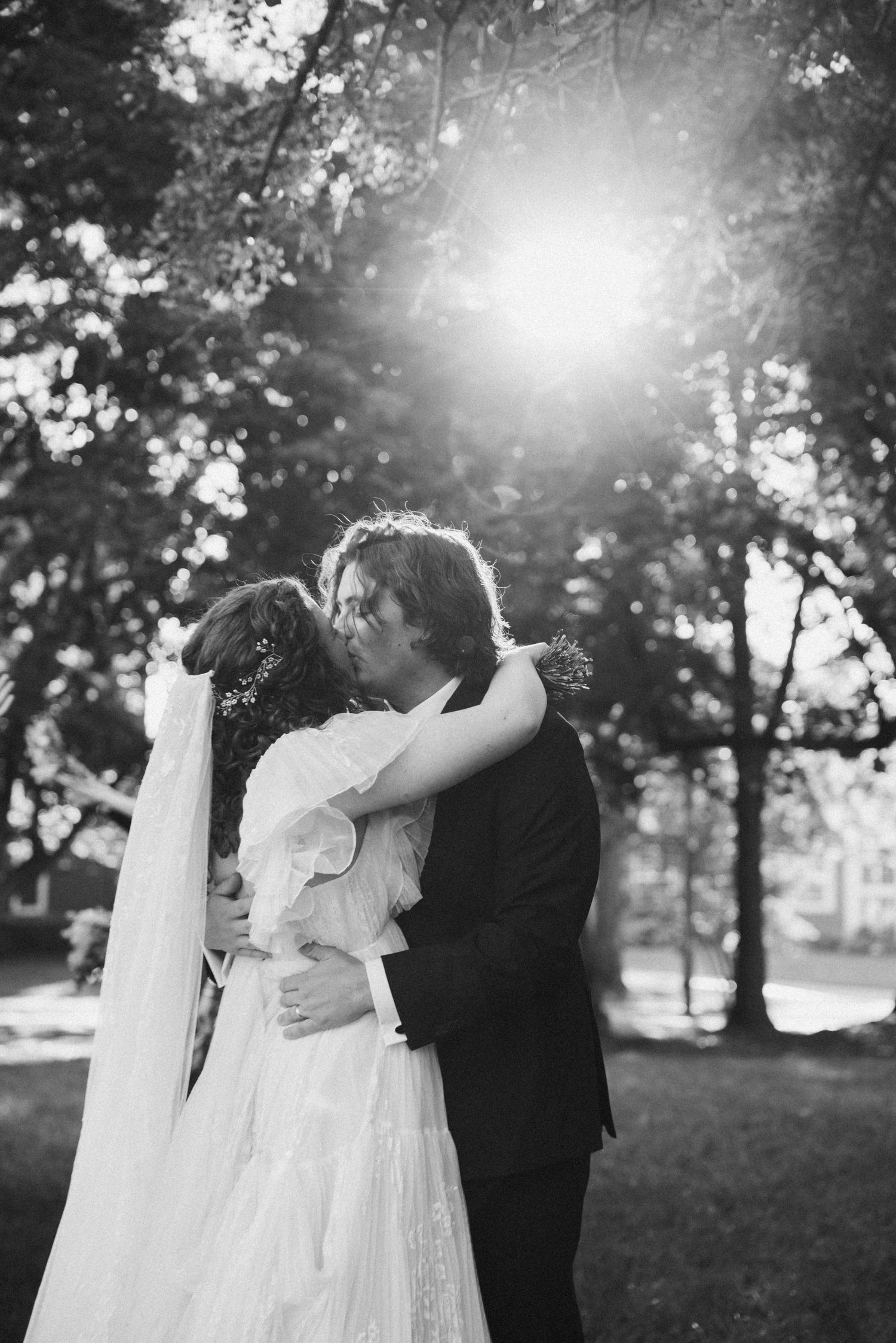 Black and white photo of a romantic wedding moment in sunlit garden setting.