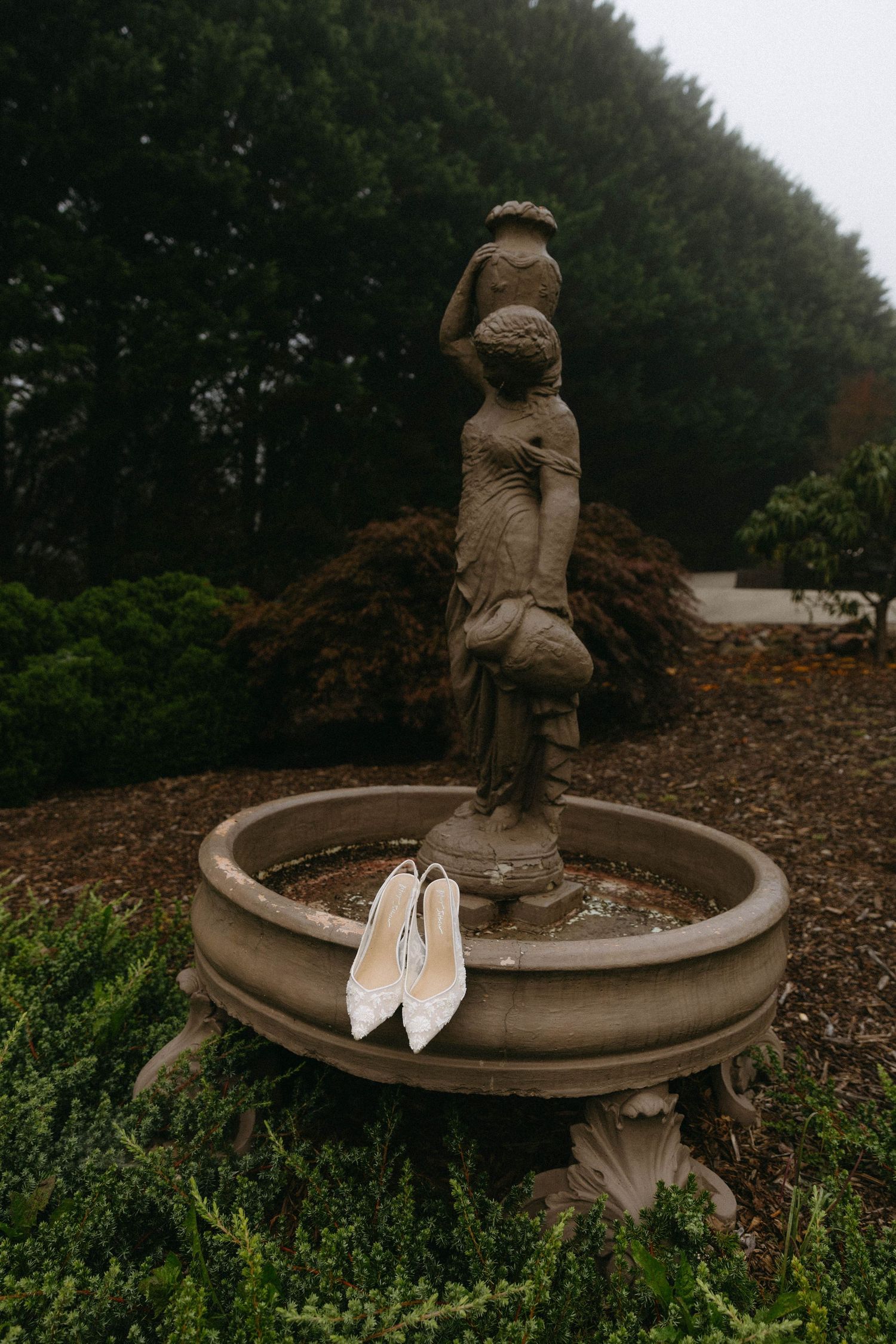 A sequence of photos showing a pair of white wedding shoes placed on a stone garden fountain with a cherub statue.