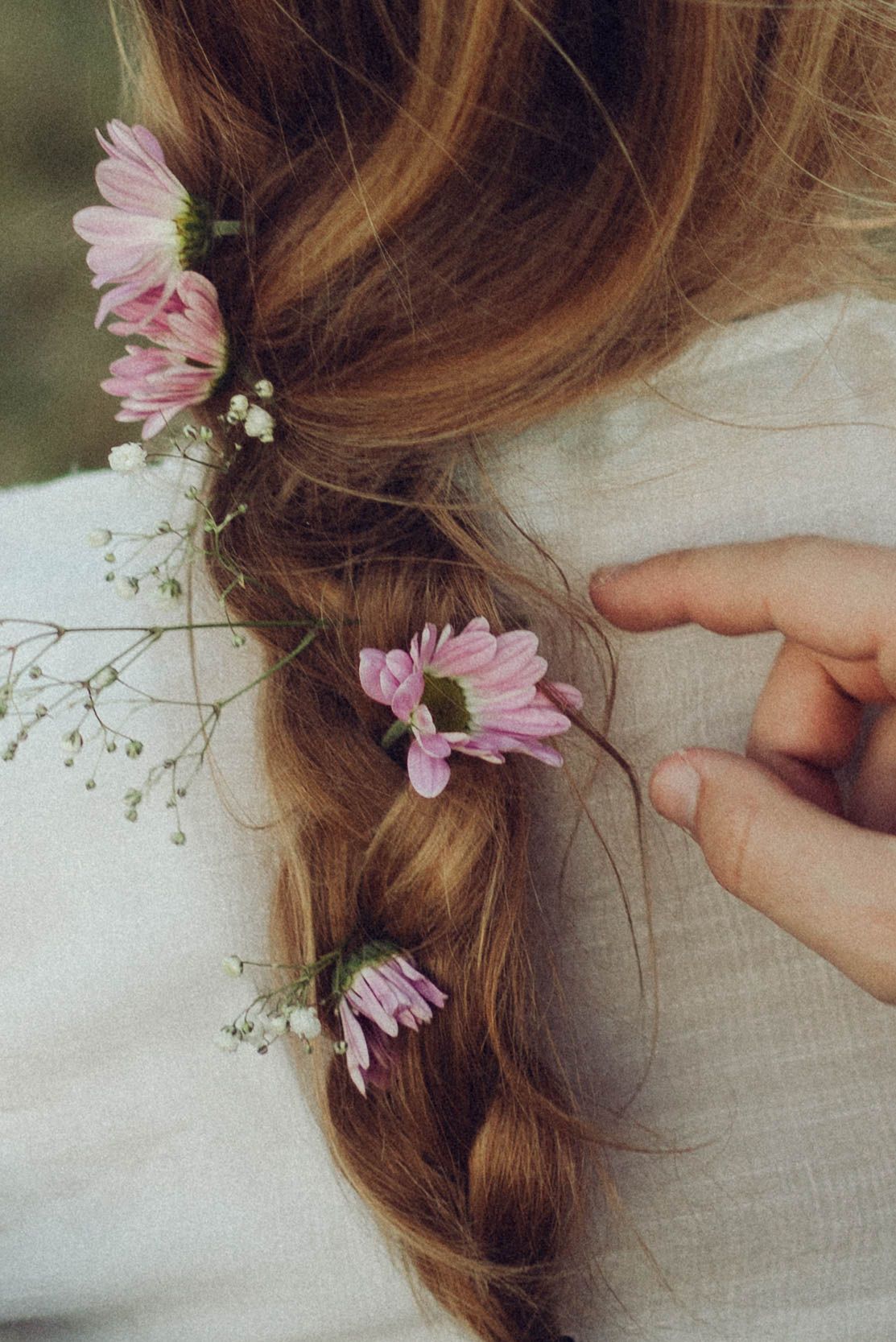 Delicate pink flowers and baby's breath being woven into a braided hairstyle.