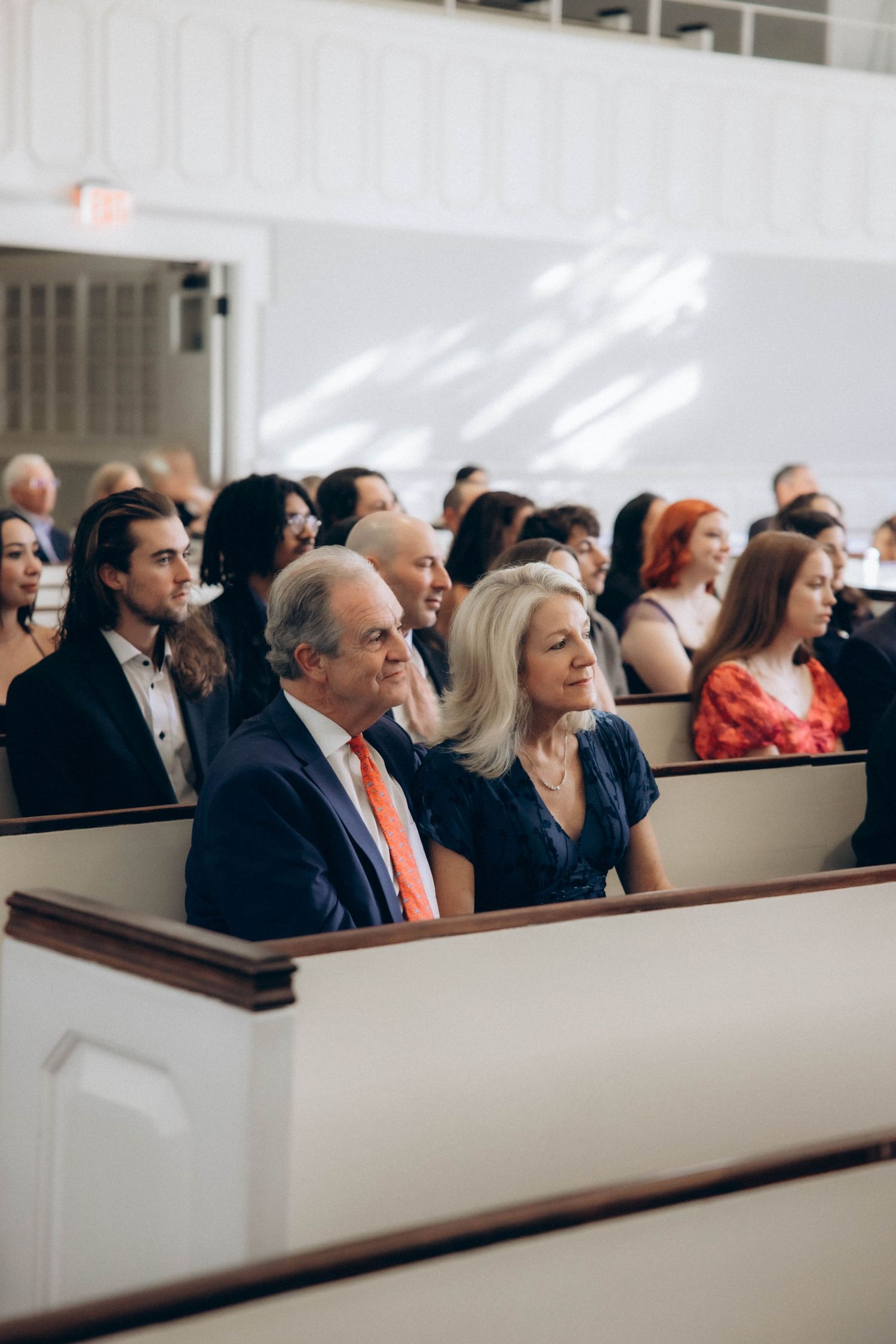 Wedding guests seated in traditional white church pews during ceremony.