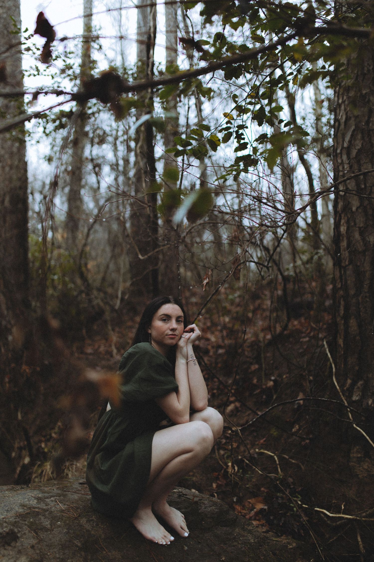 Person in dark clothing crouching in moody forest setting during autumn.