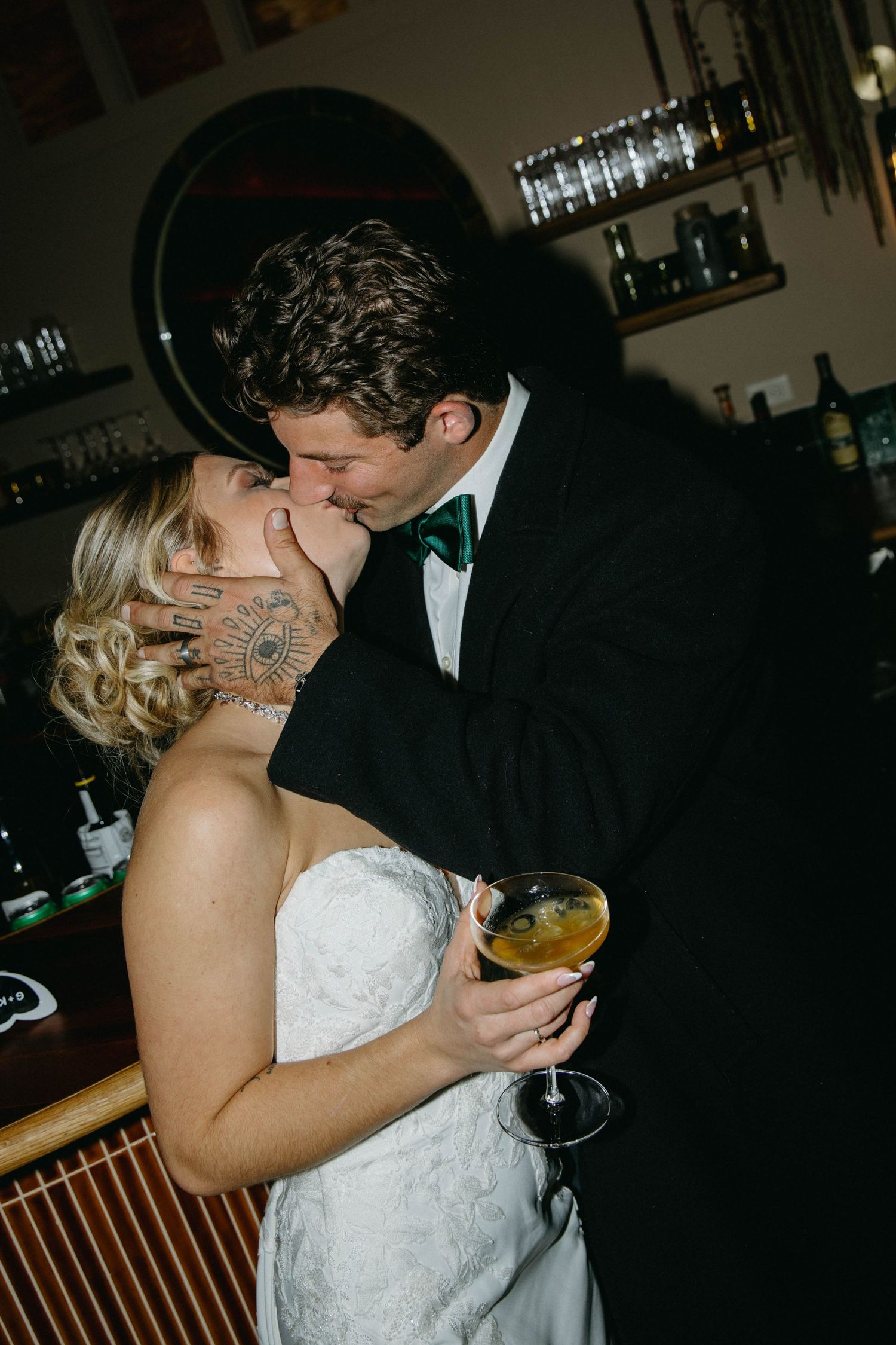 A bride and groom share a romantic kiss during their wedding reception at a dimly lit bar venue.