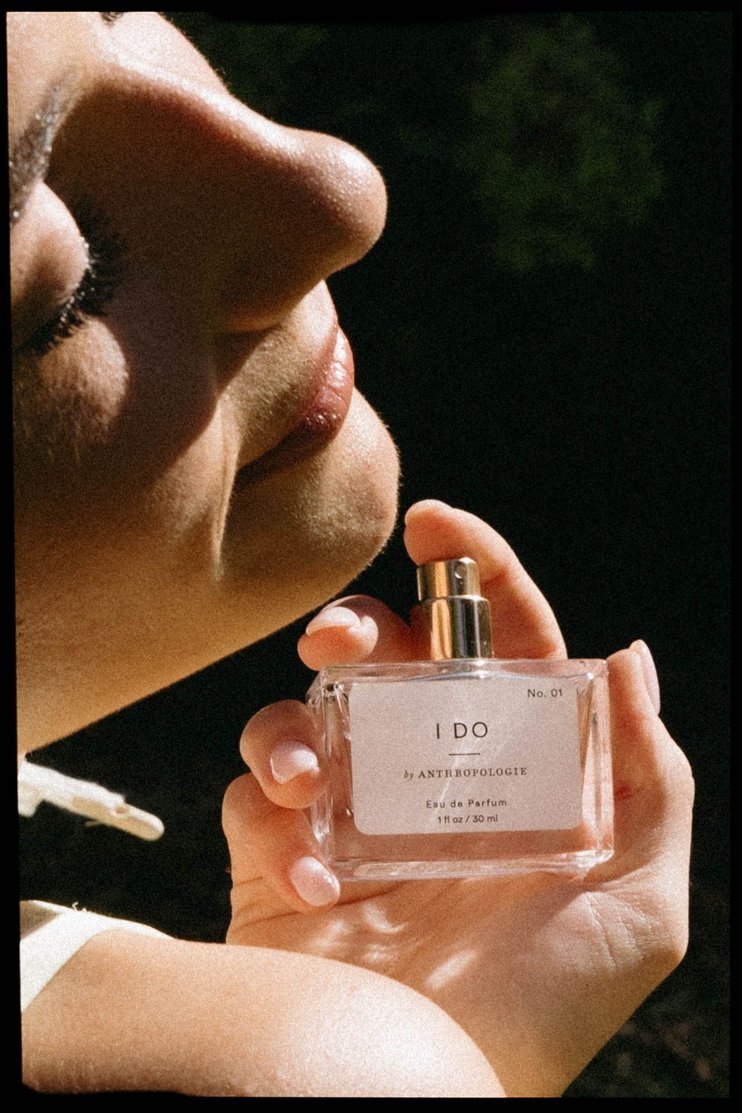 Close-up shot of hands holding a perfume bottle labeled 'I DO' against a dark background with soft lighting.