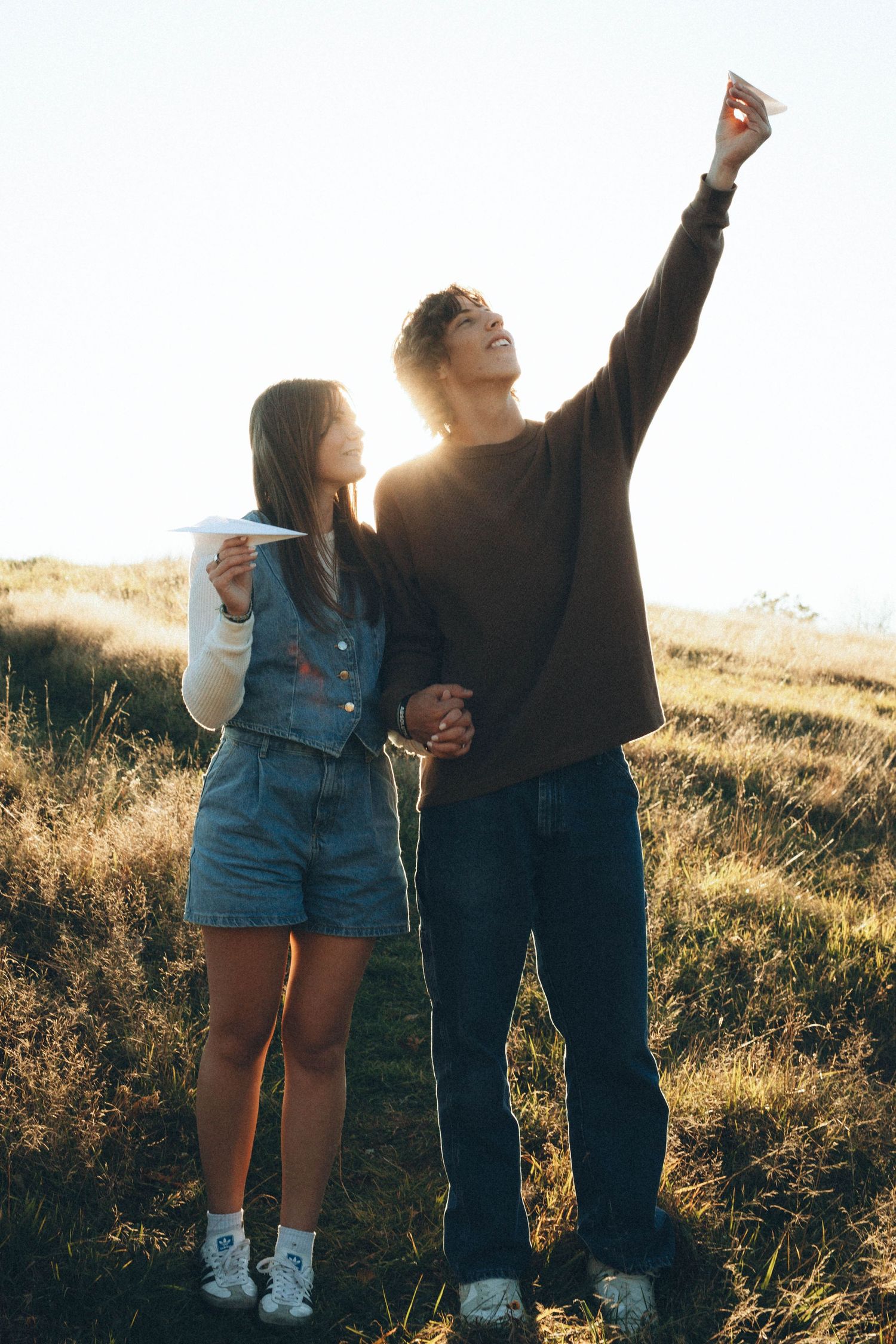 Friends celebrating in a sunlit field wearing denim and casual clothes.
