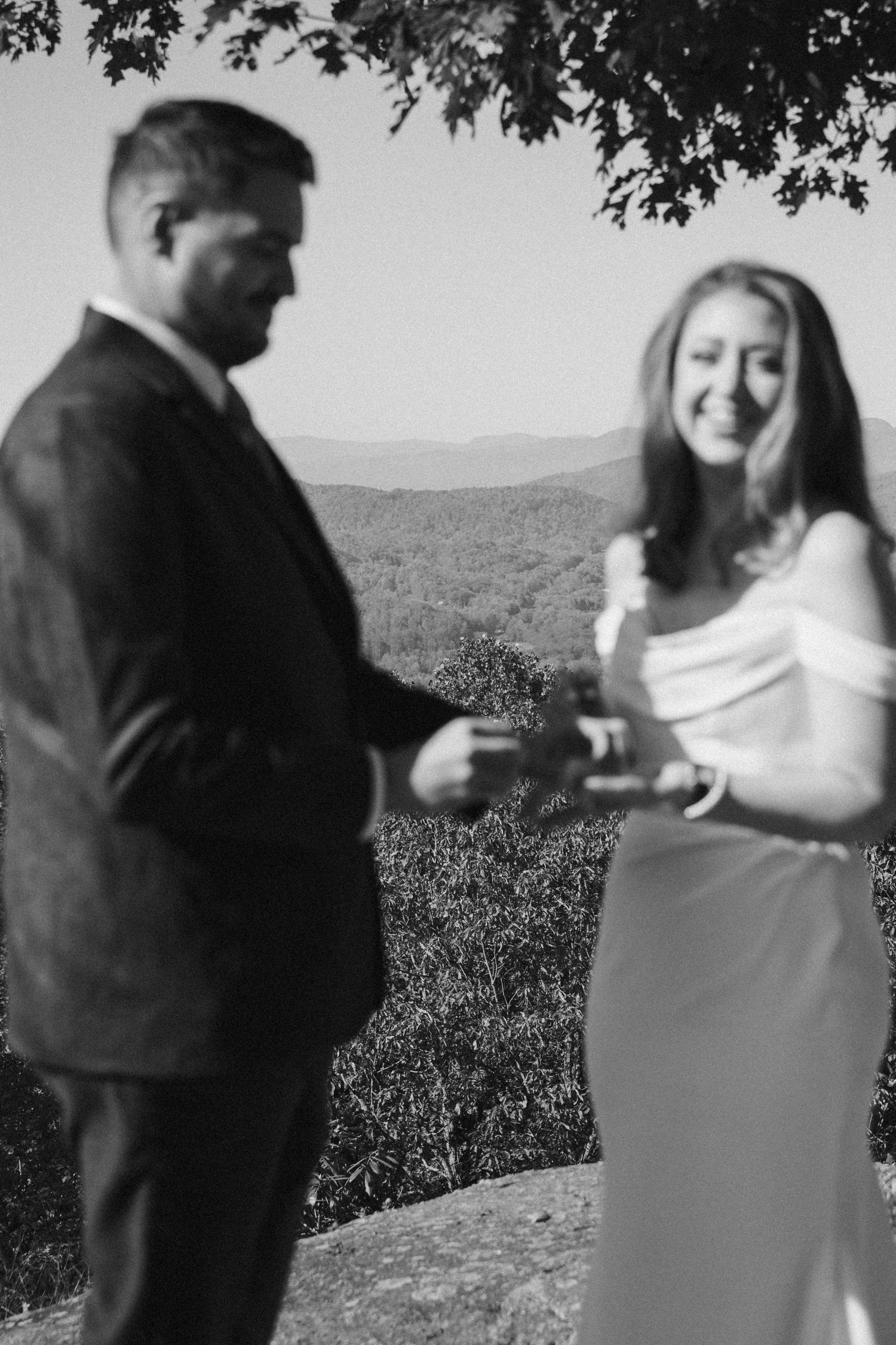 A couple in formal attire share an intimate moment together on a scenic overlook with mountains in the background.