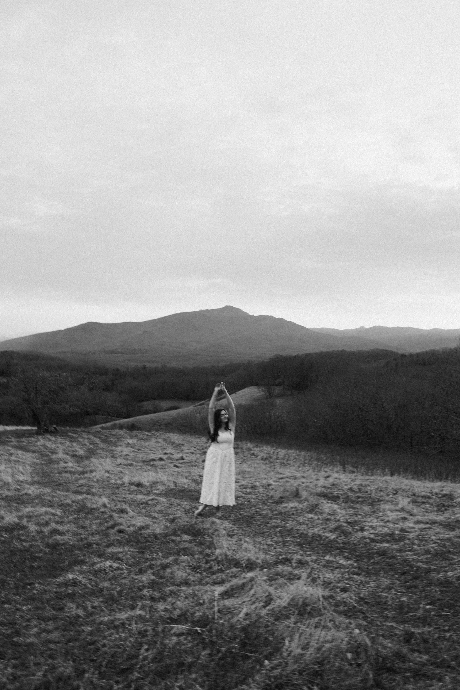 Figure in white dress silhouetted against mountain landscape in black and white photography.