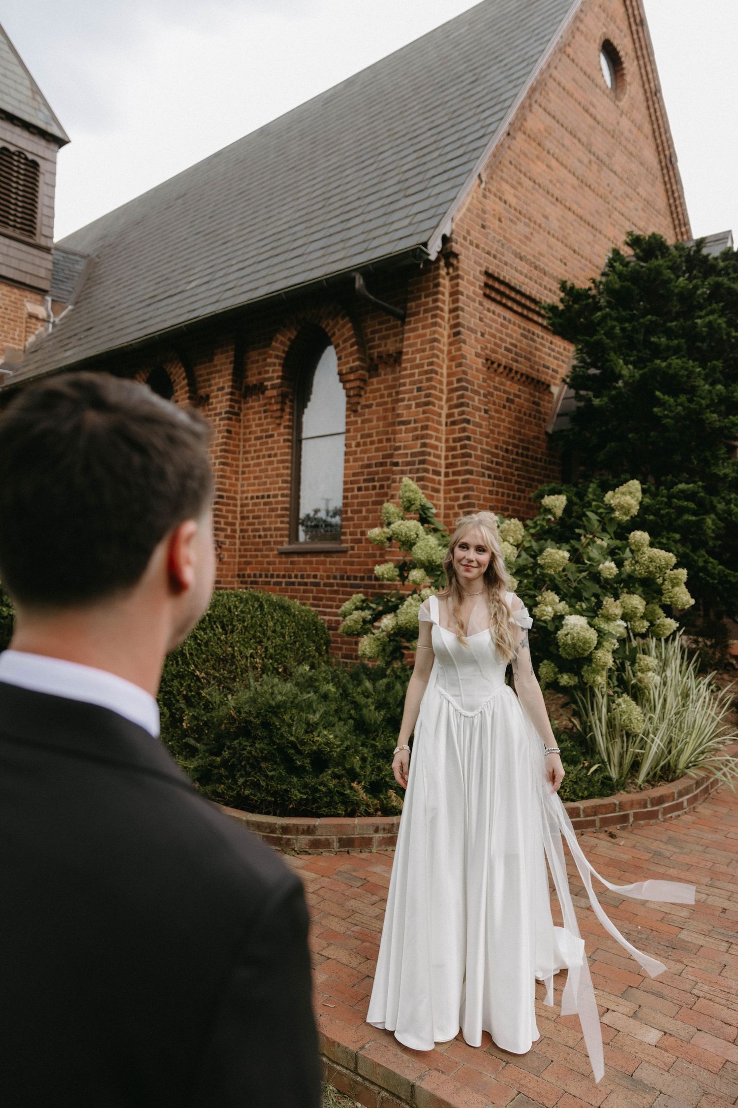 A romantic first look moment between a bride in a flowing white dress and groom at a brick church courtyard.