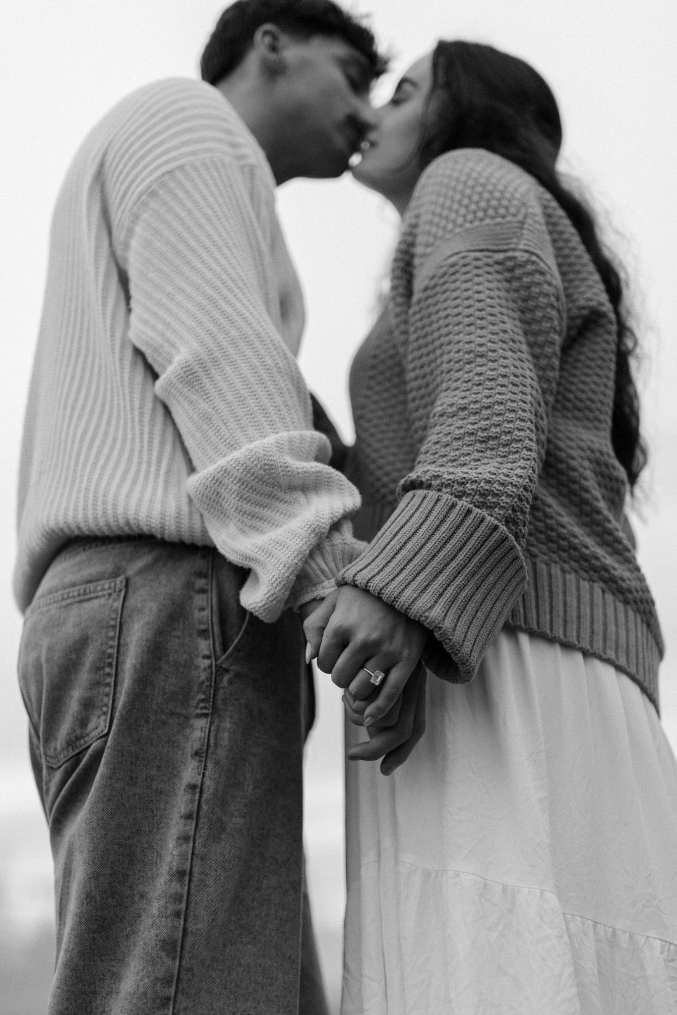 Black and white photo series showing couple in cozy sweaters holding hands intimately.