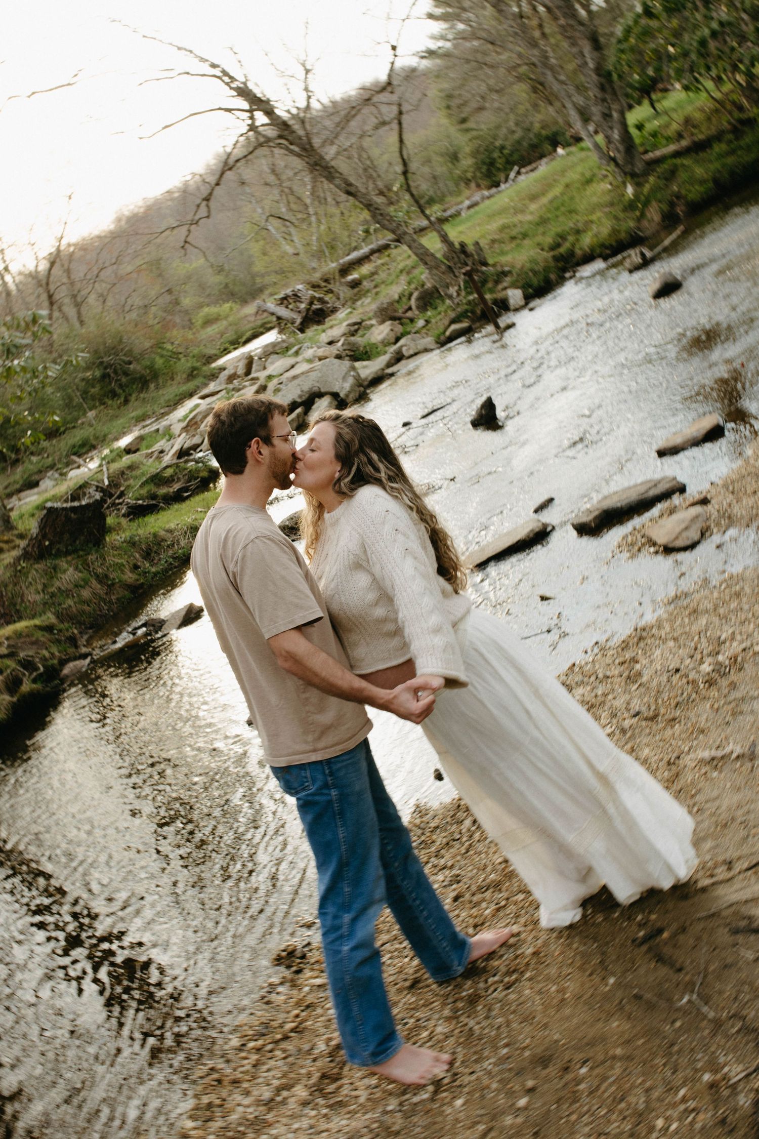 Romantic moment captured by flowing creek with natural stone and water backdrop.