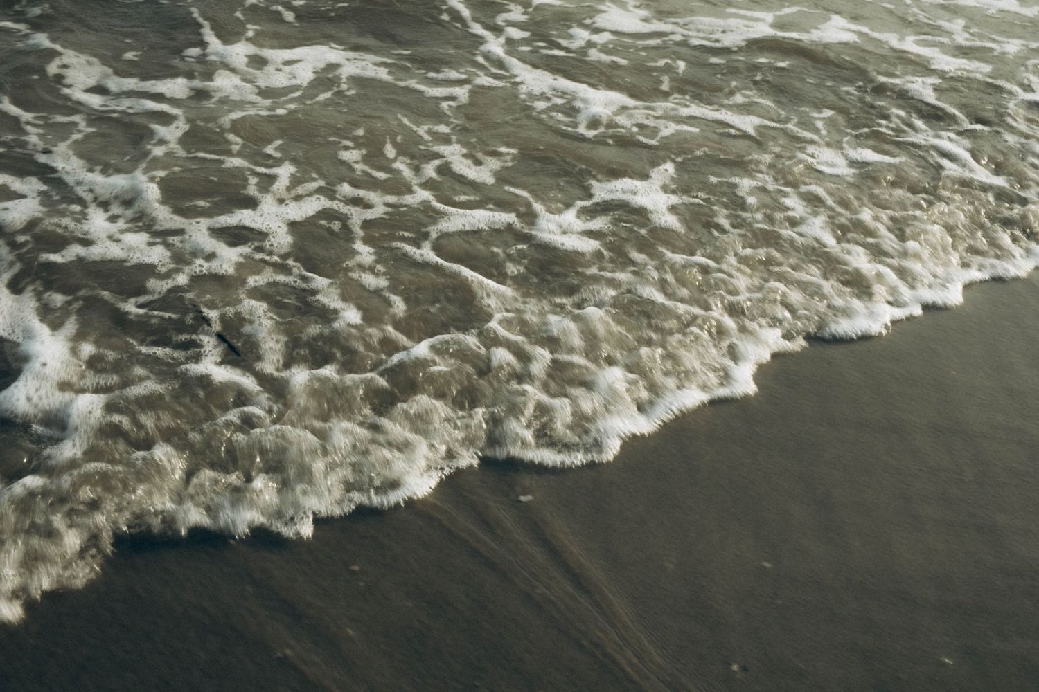 Ocean waves washing up on dark sand with white foam patterns.