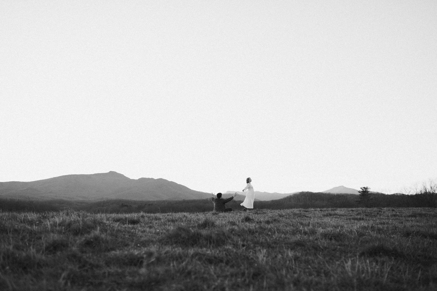 Black and white landscape photograph showing rolling hills and distant mountains.