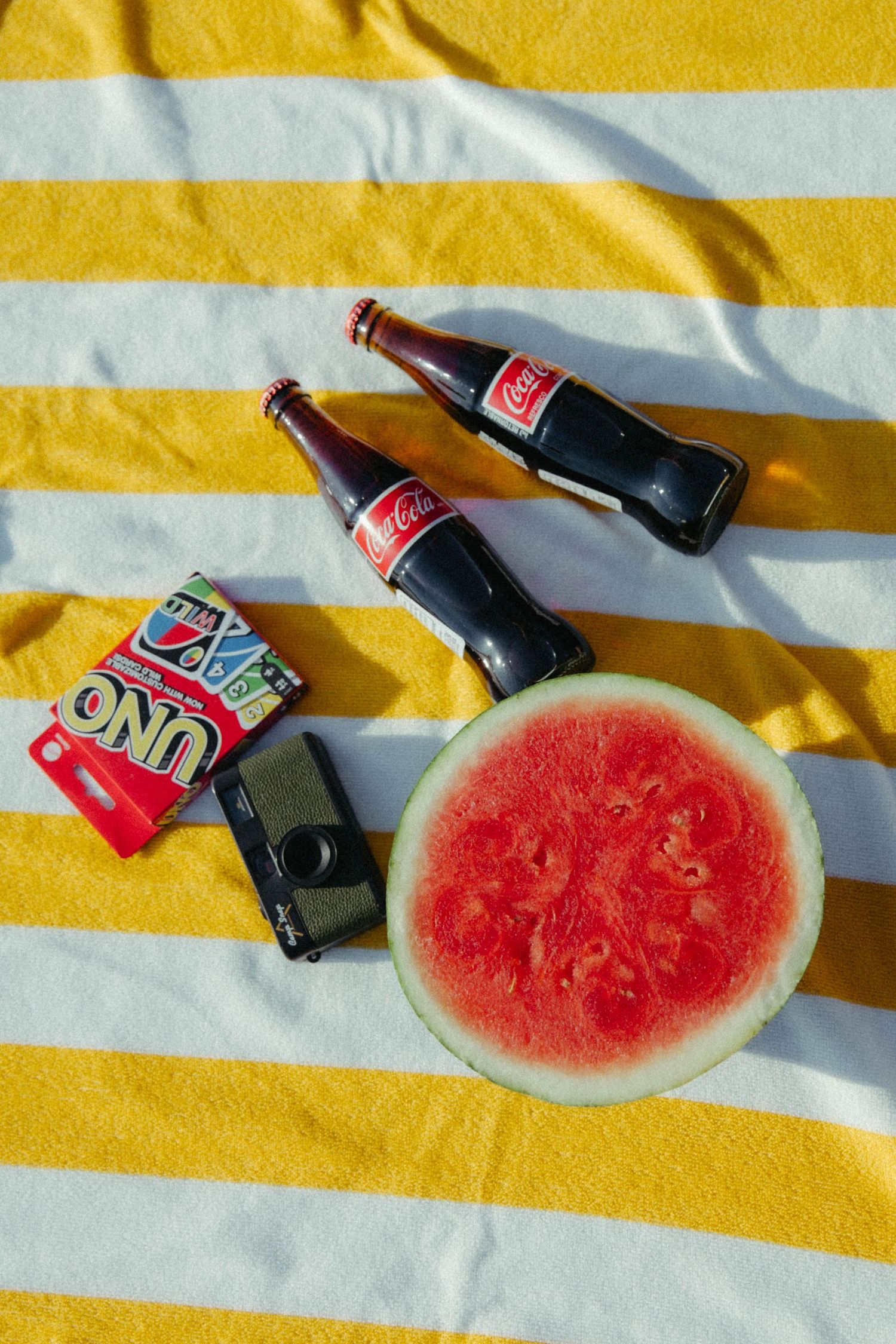 Fresh watermelon slices arranged on a yellow and white striped background with glass Coca-Cola bottles.