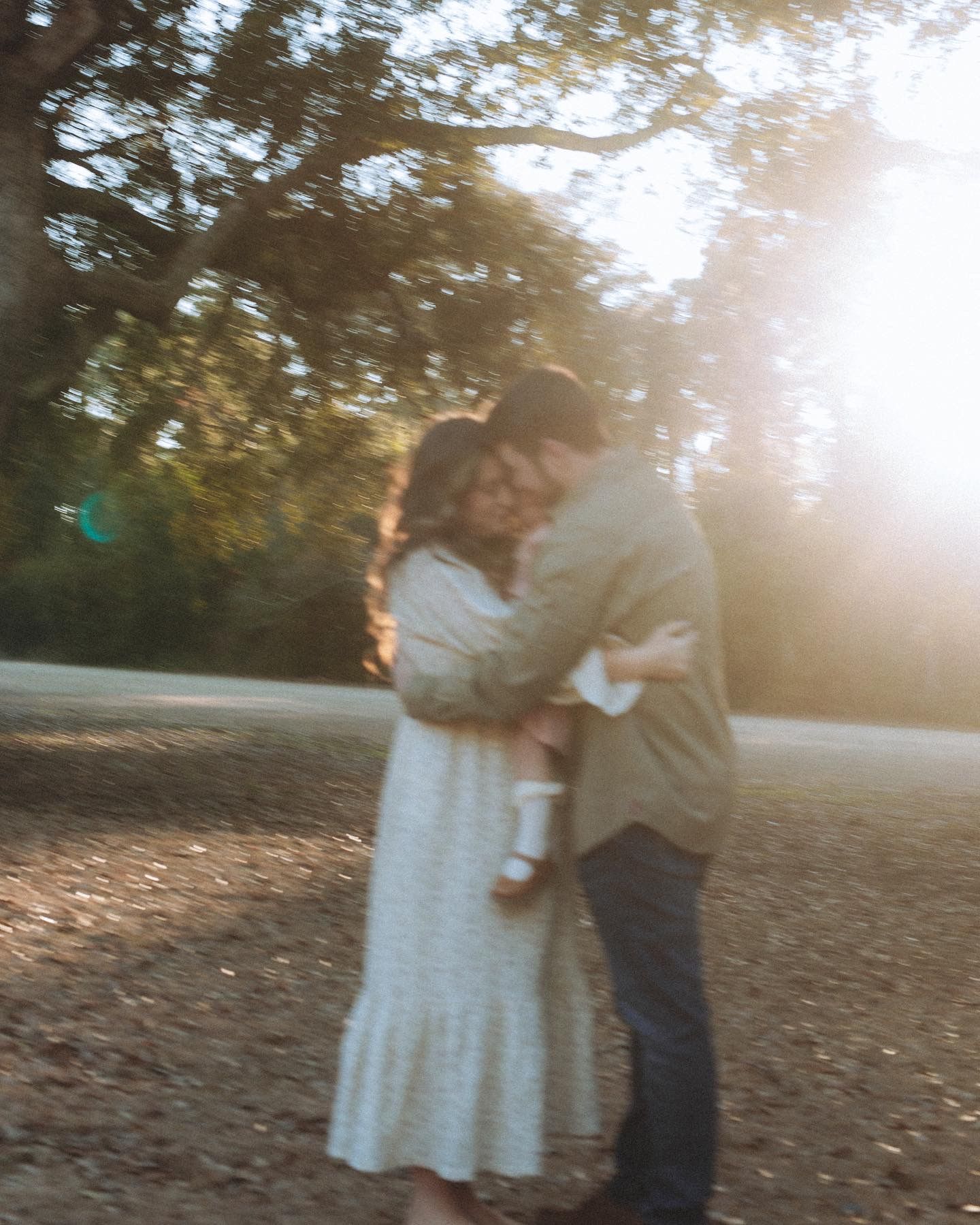 A romantic couple dancing together in a sunlit outdoor setting with fall foliage in the background.