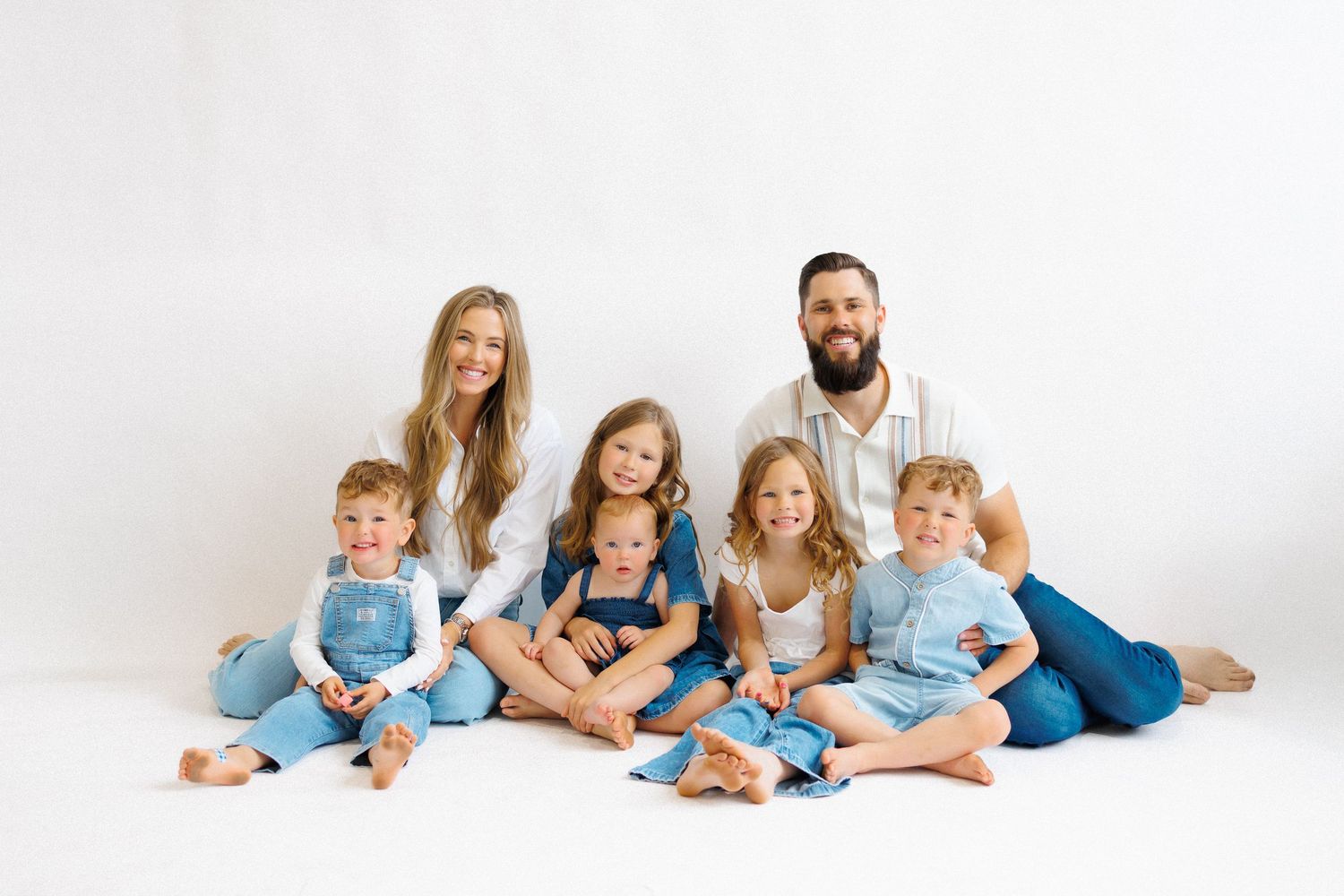 Family portrait of parents with five young children in coordinating blue and white outfits on white background.