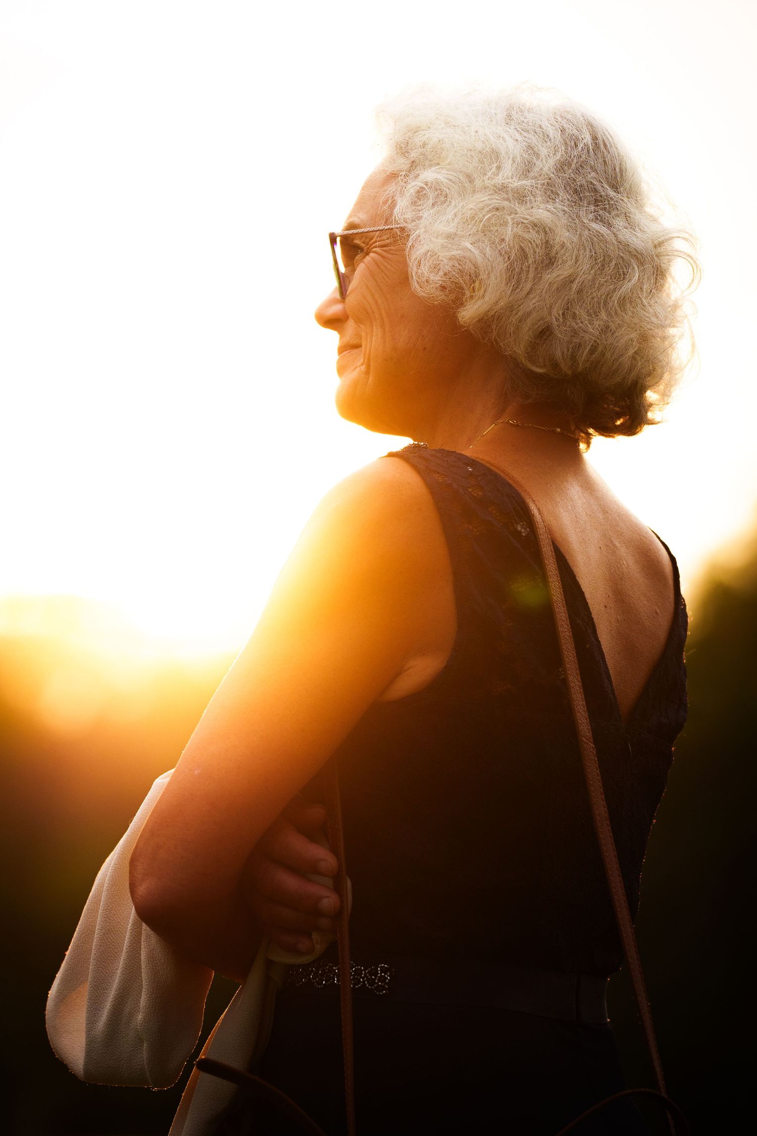 Portrait de profil d'une personne joyeuse aux cheveux gris bouclés portant des lunettes de soleil et un haut sans manches.