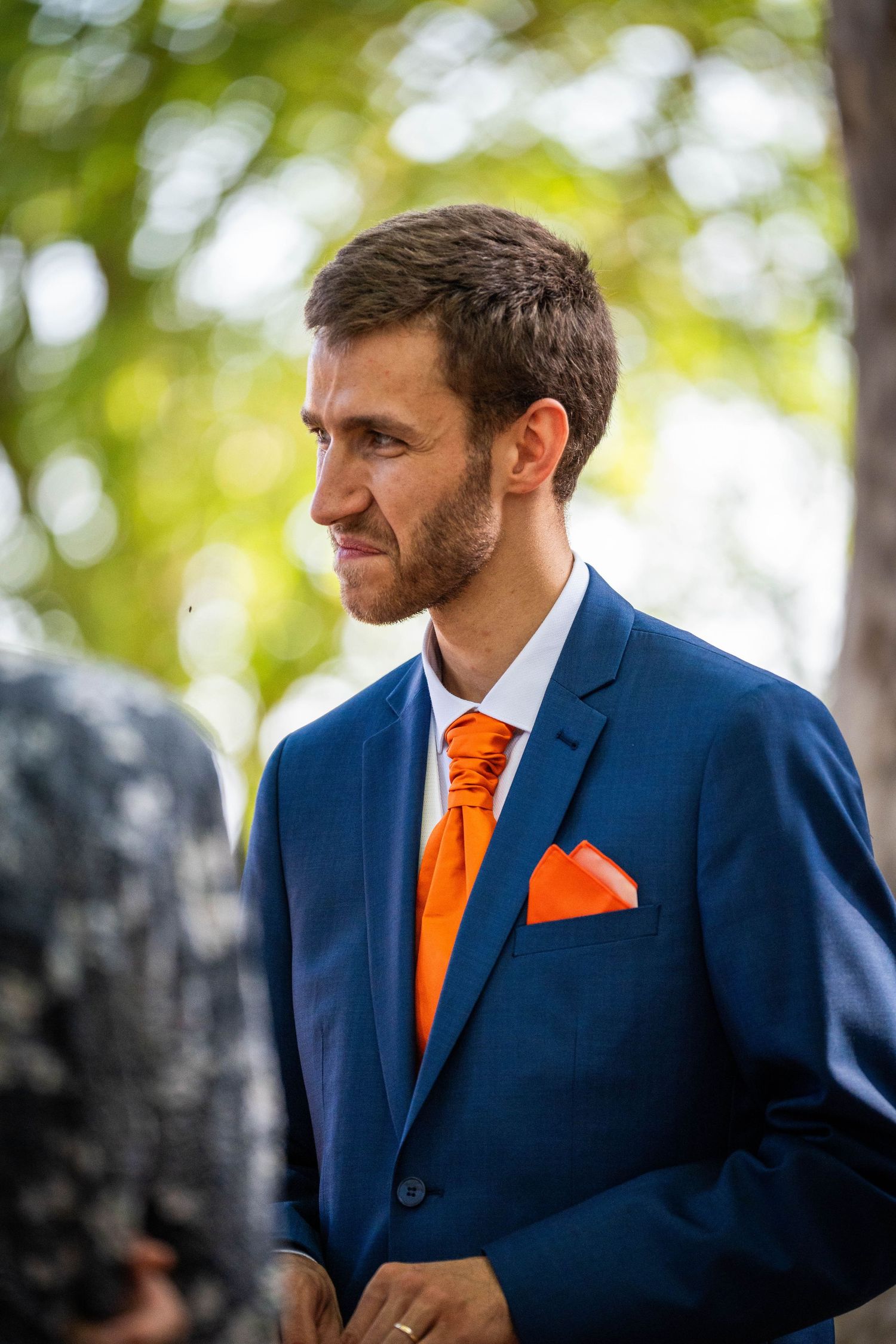 Un marié portant un costume bleu marine avec une cravate orange vif et une pochette en extérieur avec un fond vert flou.
