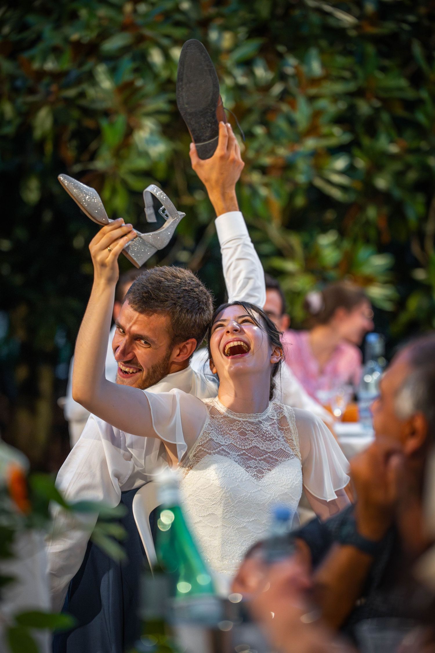 Un couple lors d'une célébration de mariage en plein air brandit joyeusement des chaussures dans le cadre d'une tradition amusante.