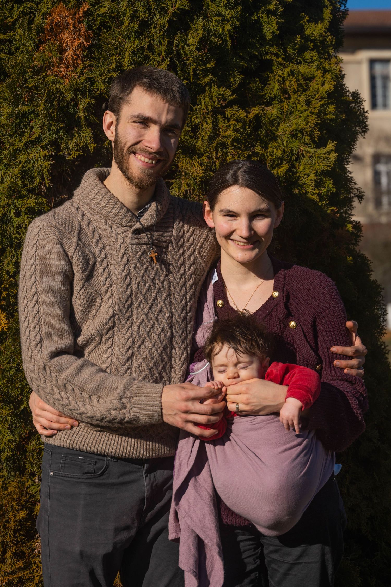Une jeune famille à l'extérieur devant un sapin lors d'une journée ensoleillée d'automne.