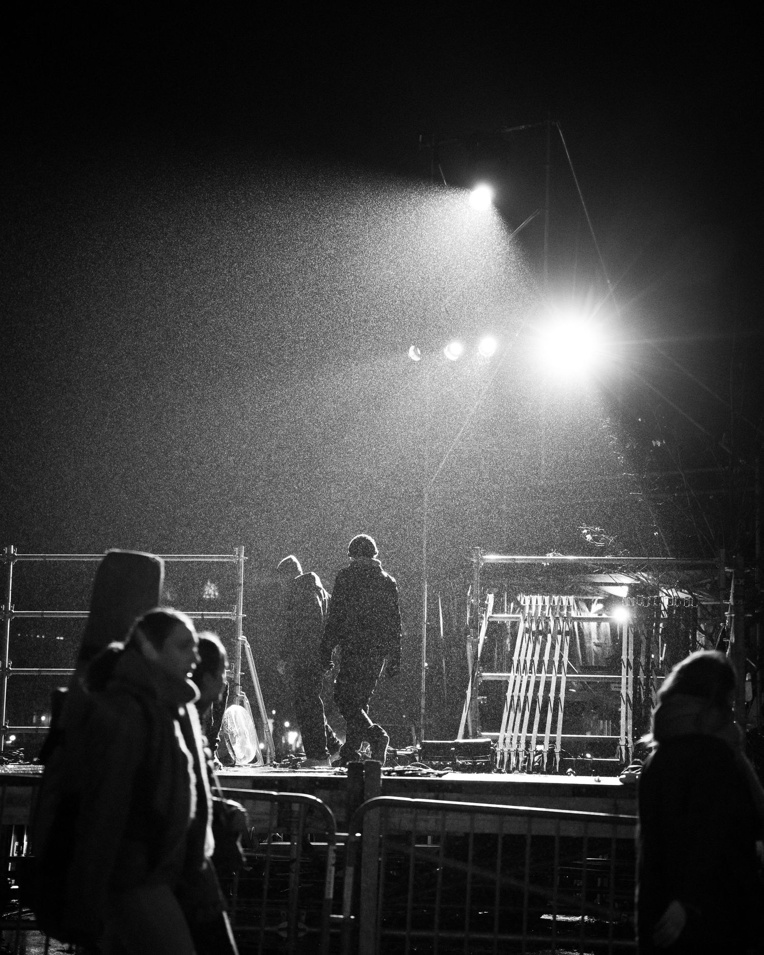 Silhouettes noires et blanches de l'équipe travaillant dans les coulisses d'un concert avec des lumières de scène lumineuses.