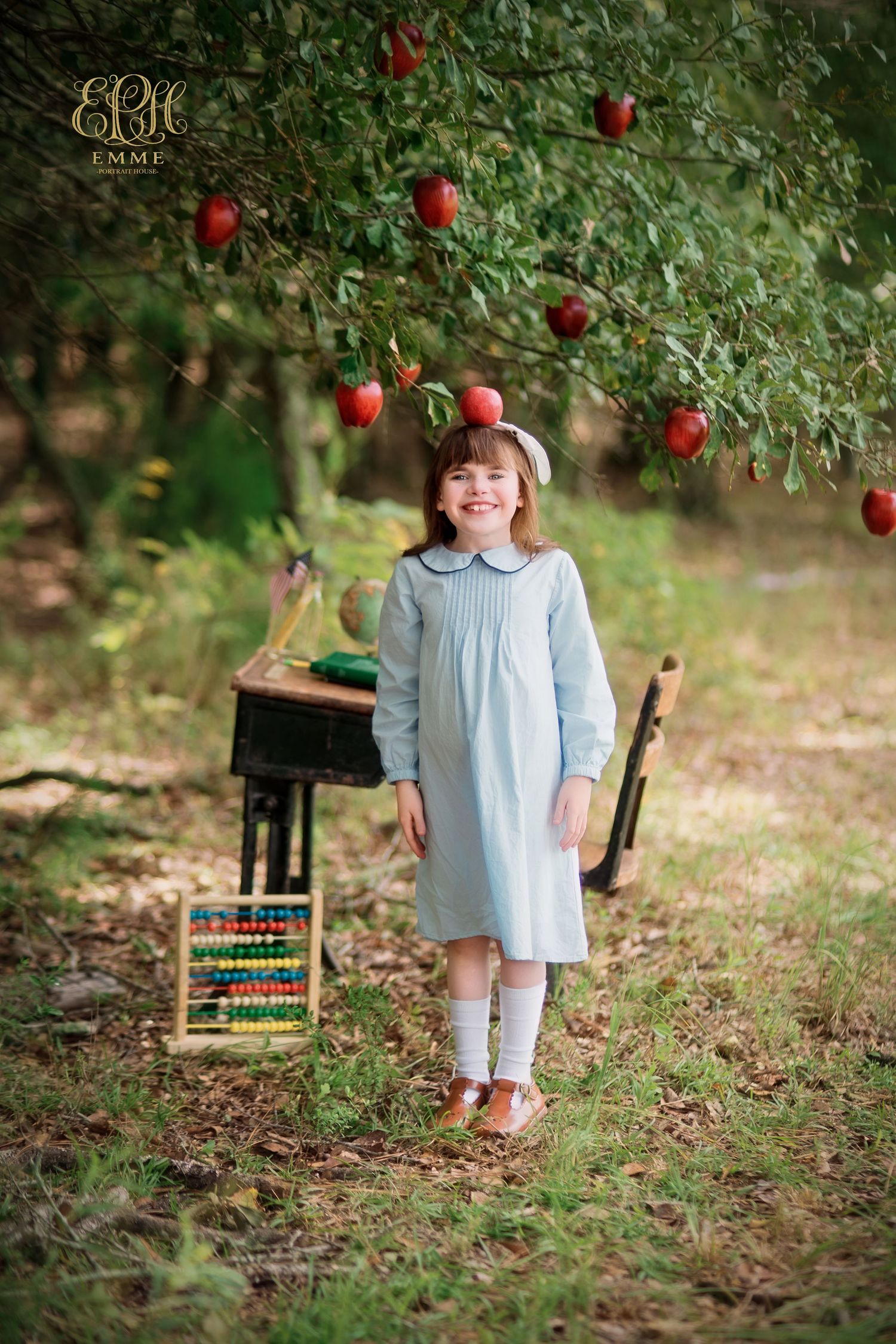 Girl in blue dress stands under apple tree with abacus and school desk in a charming back-to-school outdoor portrait in Orangeburg, SC