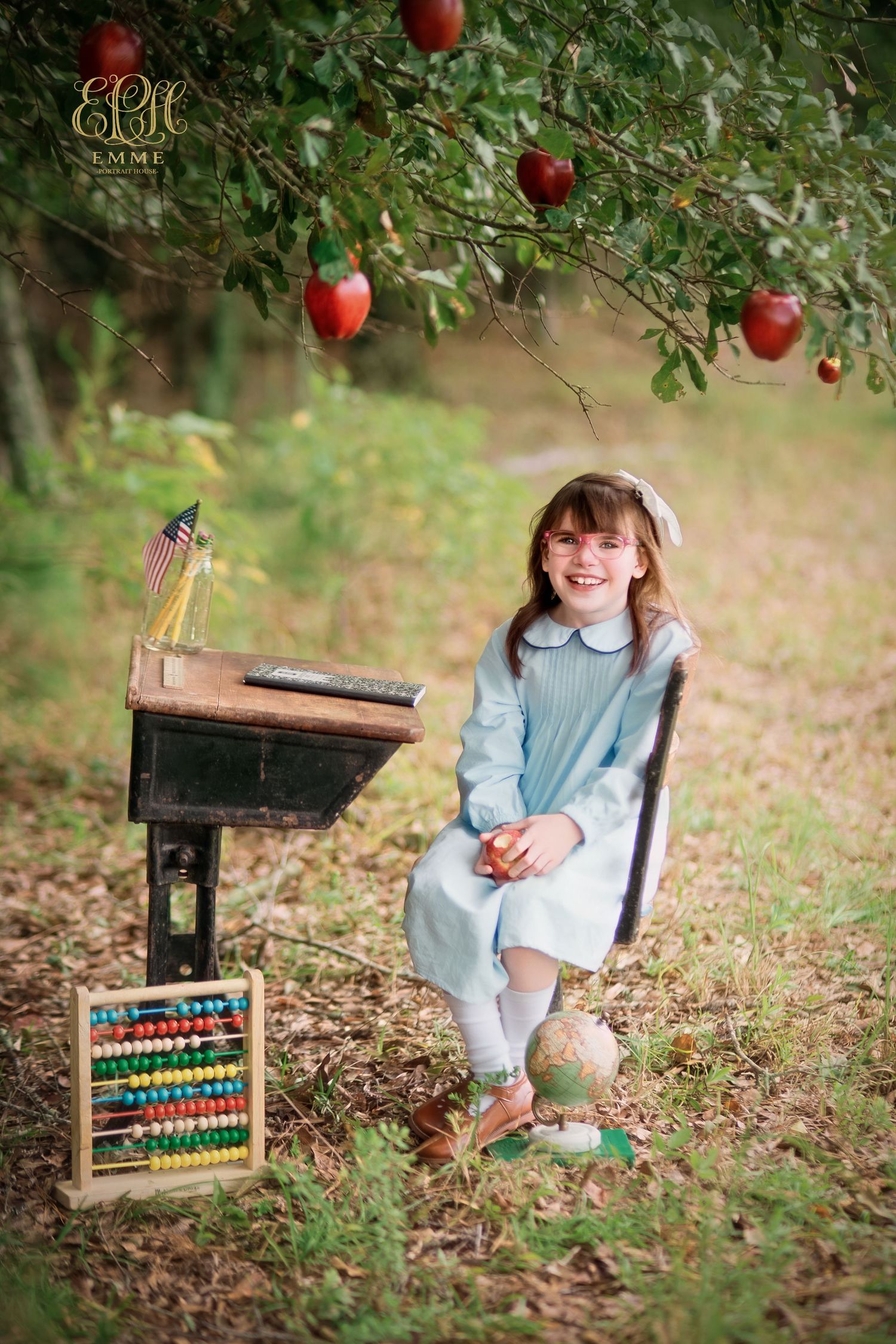 Back to school portrait of a girl in a blue dress under an apple tree with a vintage school desk in Orangeburg SC.