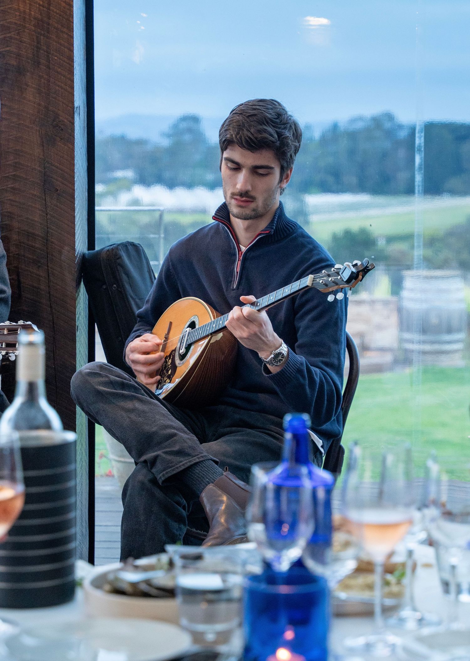 Someone playing an acoustic guitar while seated at a dining table with scenic views.